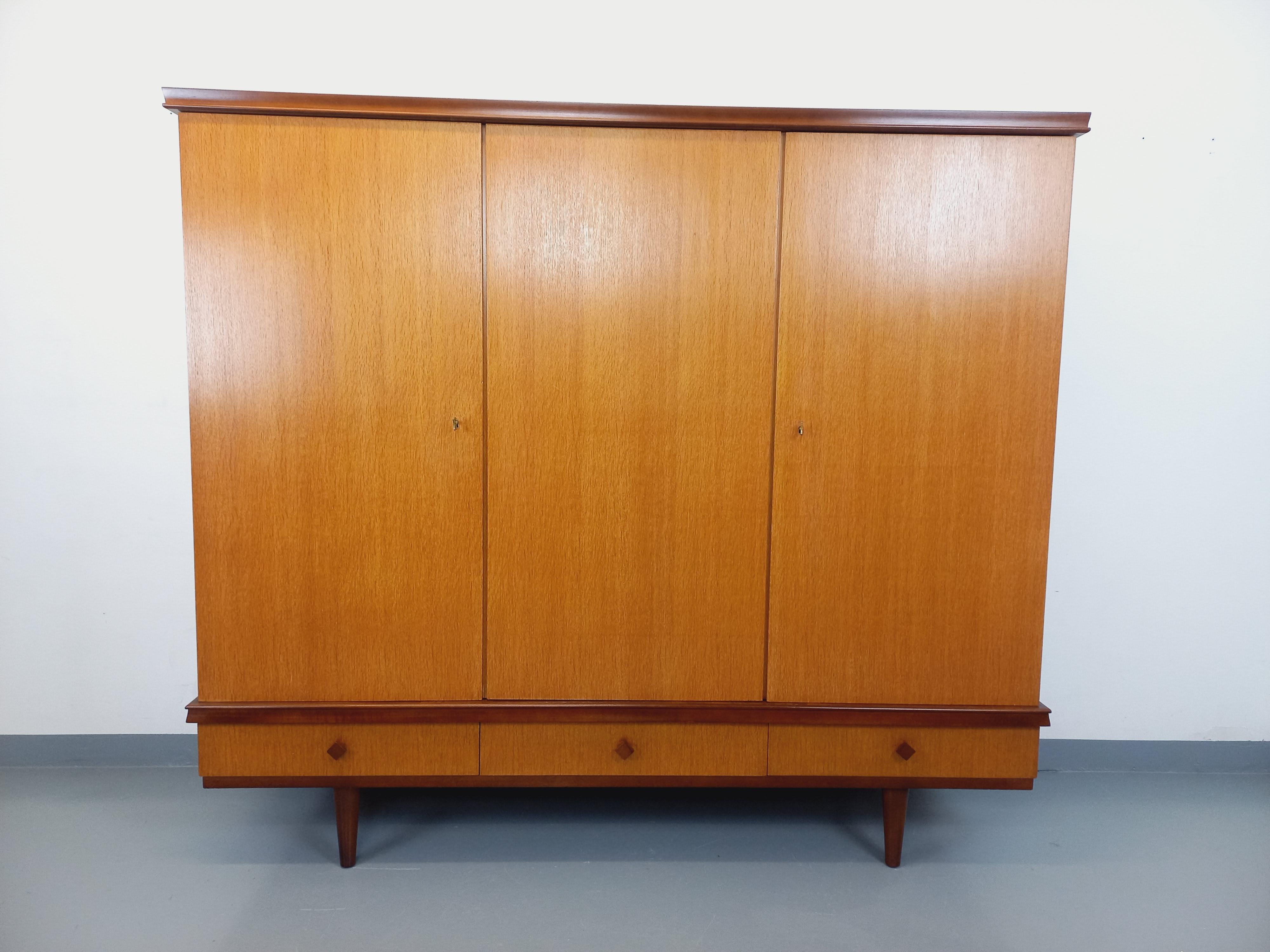 Armoire vintage des années 60 Gaston Poisson, en bois, 3 tiroirs et 3 portes avec 2 clés siglées GP en laiton. Beaucoup de rangements : 3 tiroirs ; 2 portes avec penderie, étagère et un grand miroir ; 1 partie avec 7 étagères intérieures et 6