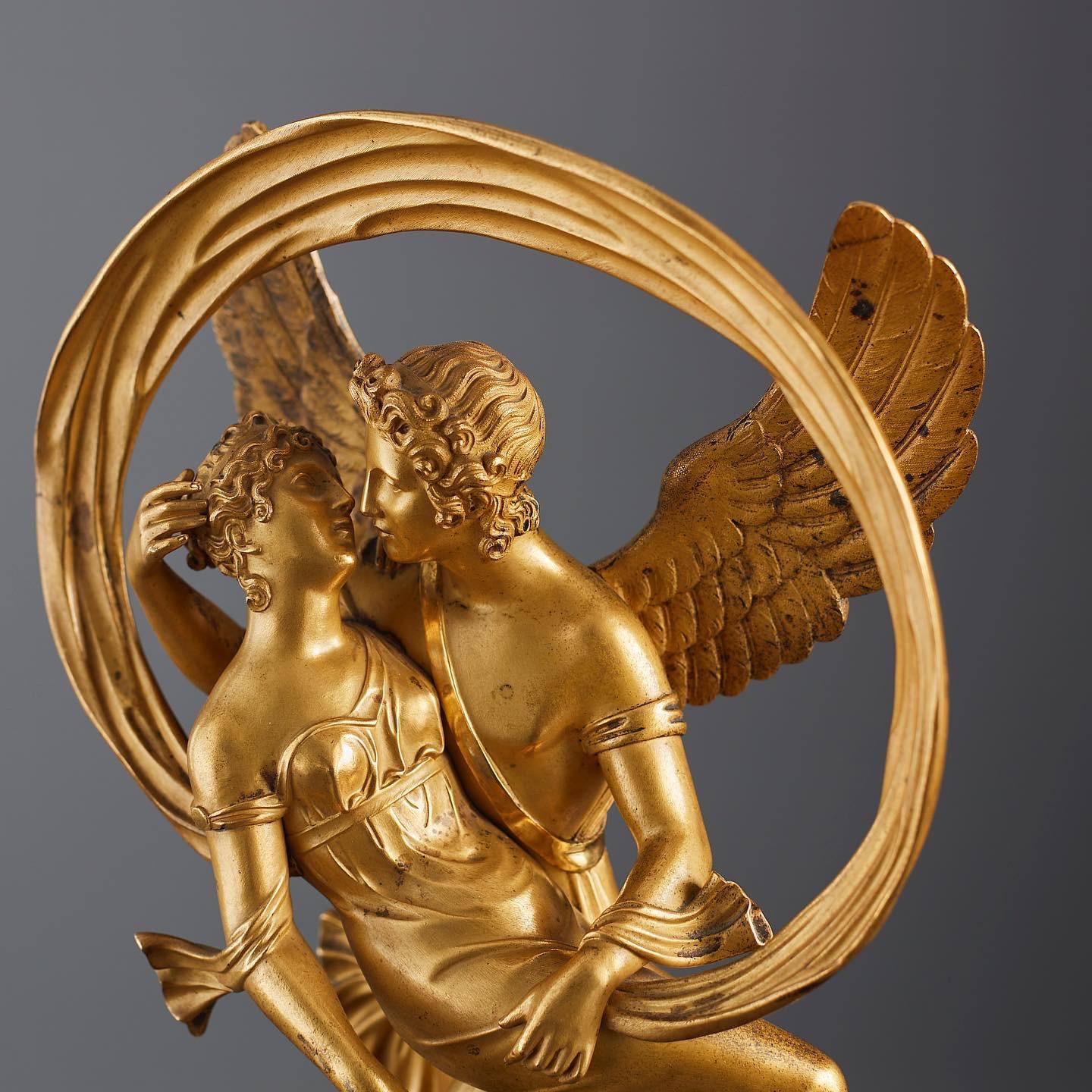 Cette belle sculpture en bronze de style Empire représente Amor ailé portant Vénus, qui tient une couronne dans sa main droite, entourée d'une étoffe circulaire au vent. Bronze doré finement ciselé sur un piédestal en marbre (marbre ver de mer).