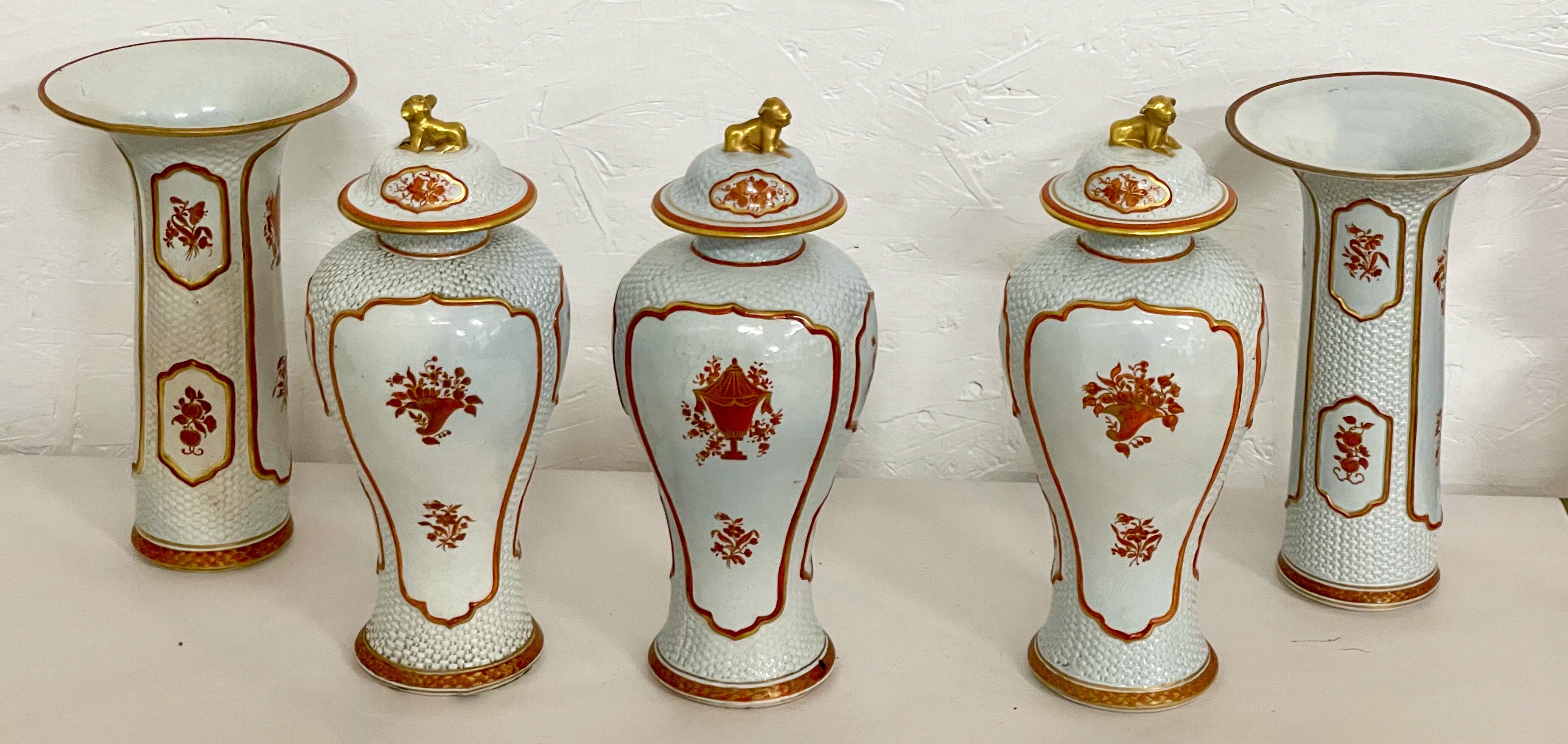 This is a lovely Asian inspired armorial garniture set with two vases and three ginger jars. They have vibrant coloration in coral and gilt. They set is marked.