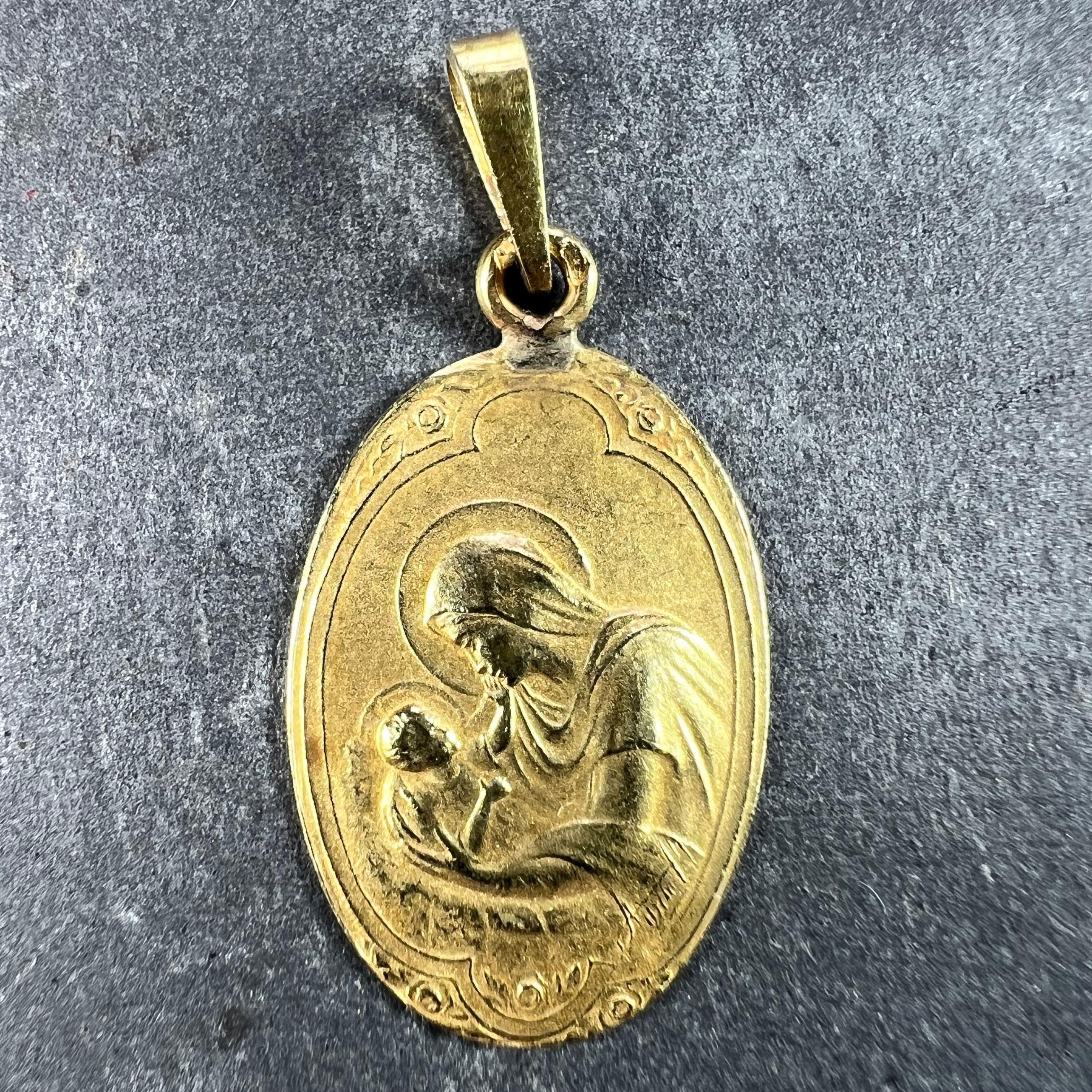 A French 18 karat (18K) yellow gold oval charm pendant designed as a medal depicting the Virgin Mary as the Madonna and Child within an Art Nouveau style frame with roses. Signed Arnault. Stamped with the eagle’s head for French manufacture and 18