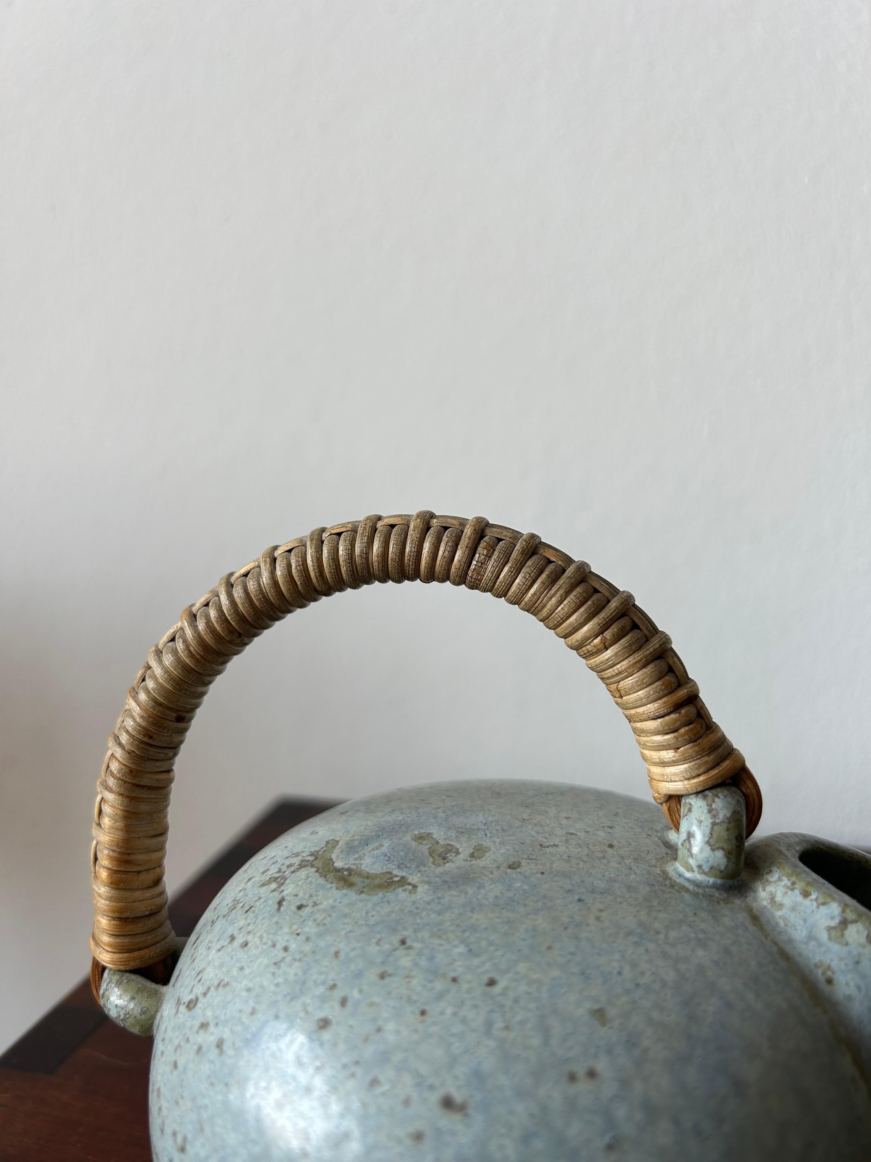 Rare and unique ceramic pitcher by Danish ceramic artist Arne Bang made at the Holmegaard workshop in the 1940’s.
The pitcher is made of glazed ceramic and has a handle made of steam bent bamboo and covered in rattan.

Arne Bang (born 29 December
