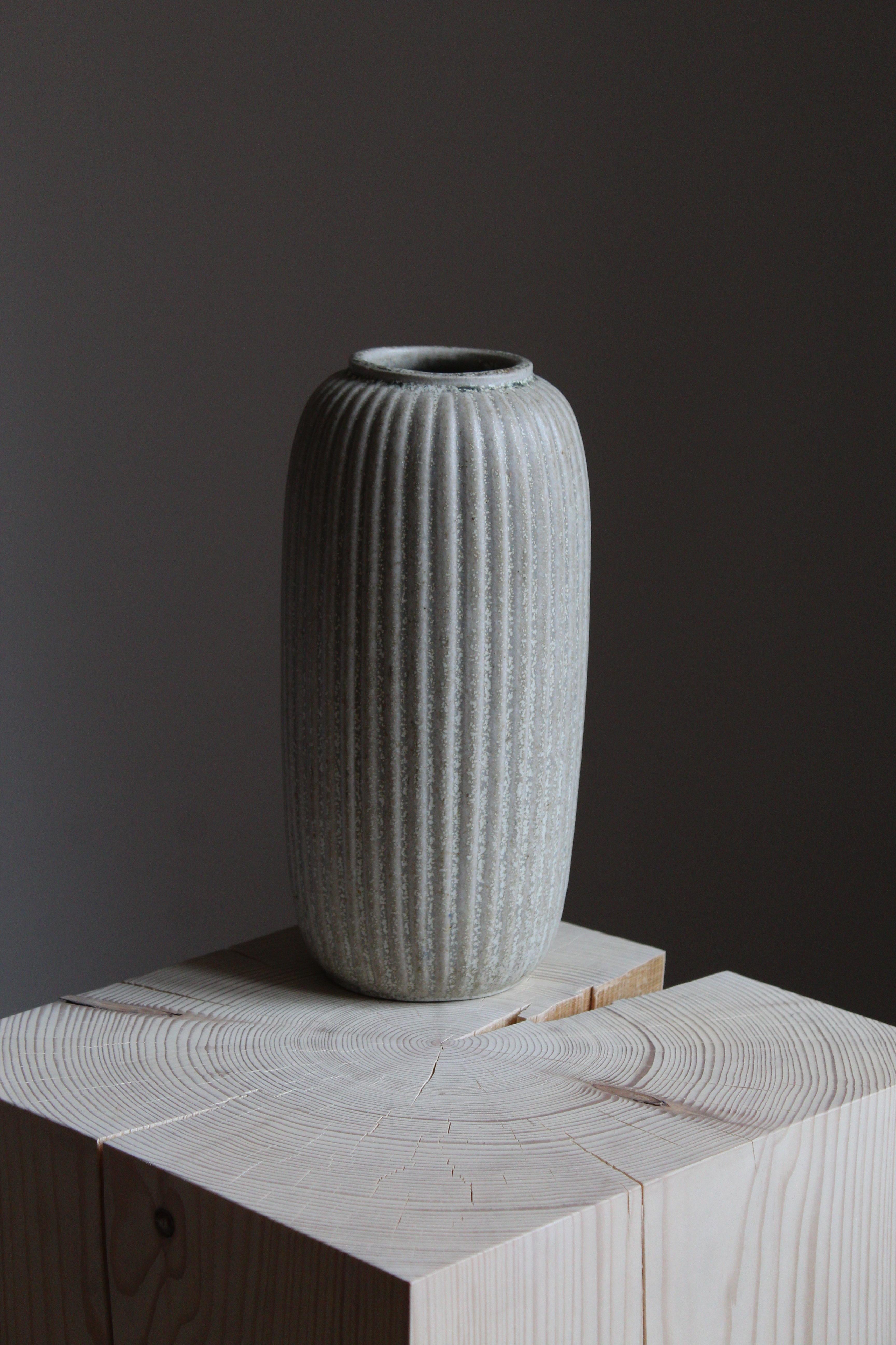 An early and sizable vase. Designed by Arne Bang, produced c. 1927. Light-grey glazed stoneware. Features ornamental ridges iconic to Bangs production.

Other designers of the period include Axel Salto, Wilhelm Kåge, Gunnar Nylund, Berndt Friberg,