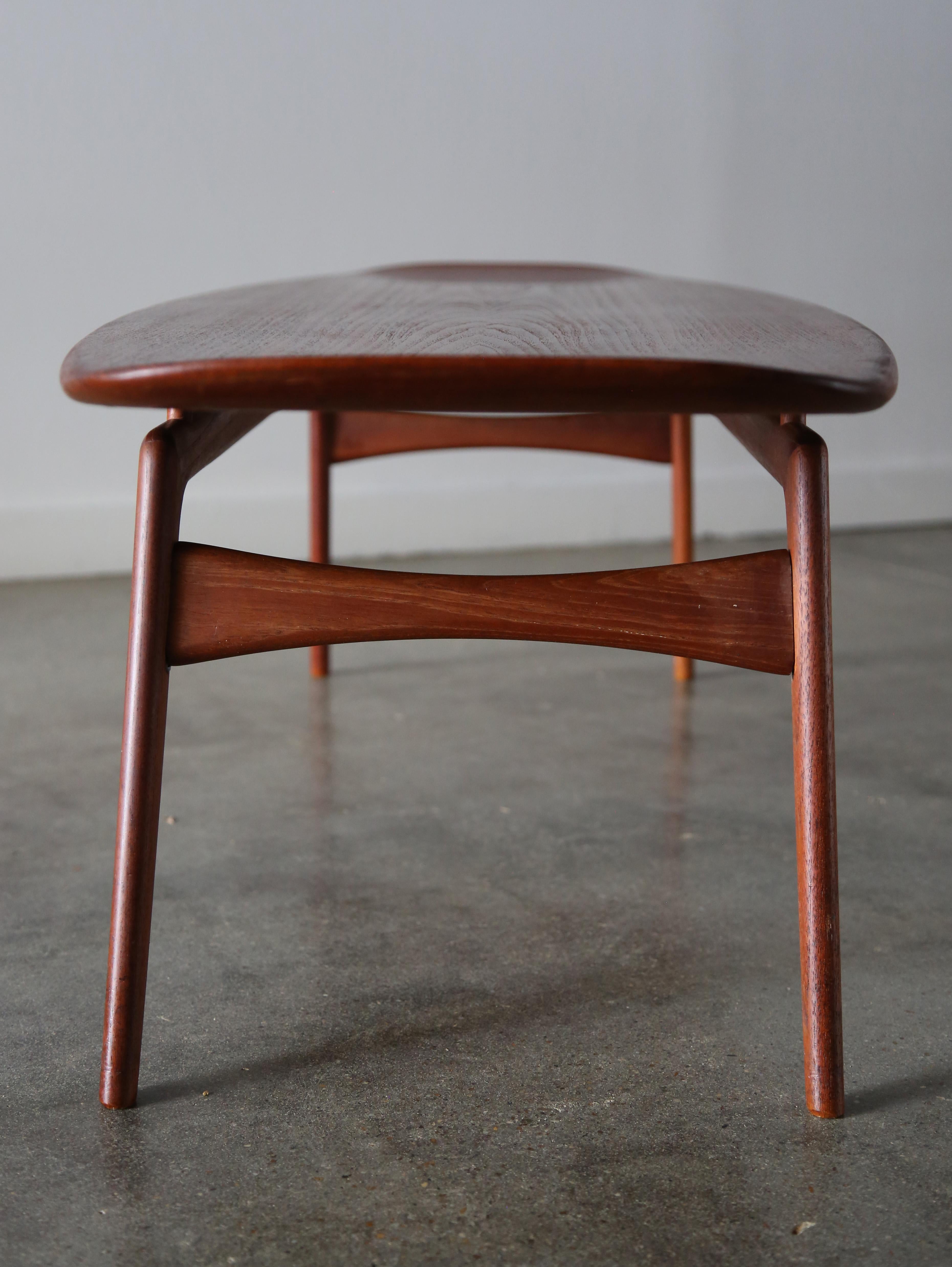 An elegant coffee table designed by Arne Hovmand Olsen for Mogens Koch. Uncommon form featuring solid teak legs and a teak veneer top. The top floats above the base on four dowels. the top is framed in solid teak with sculpted ends. A great coastal