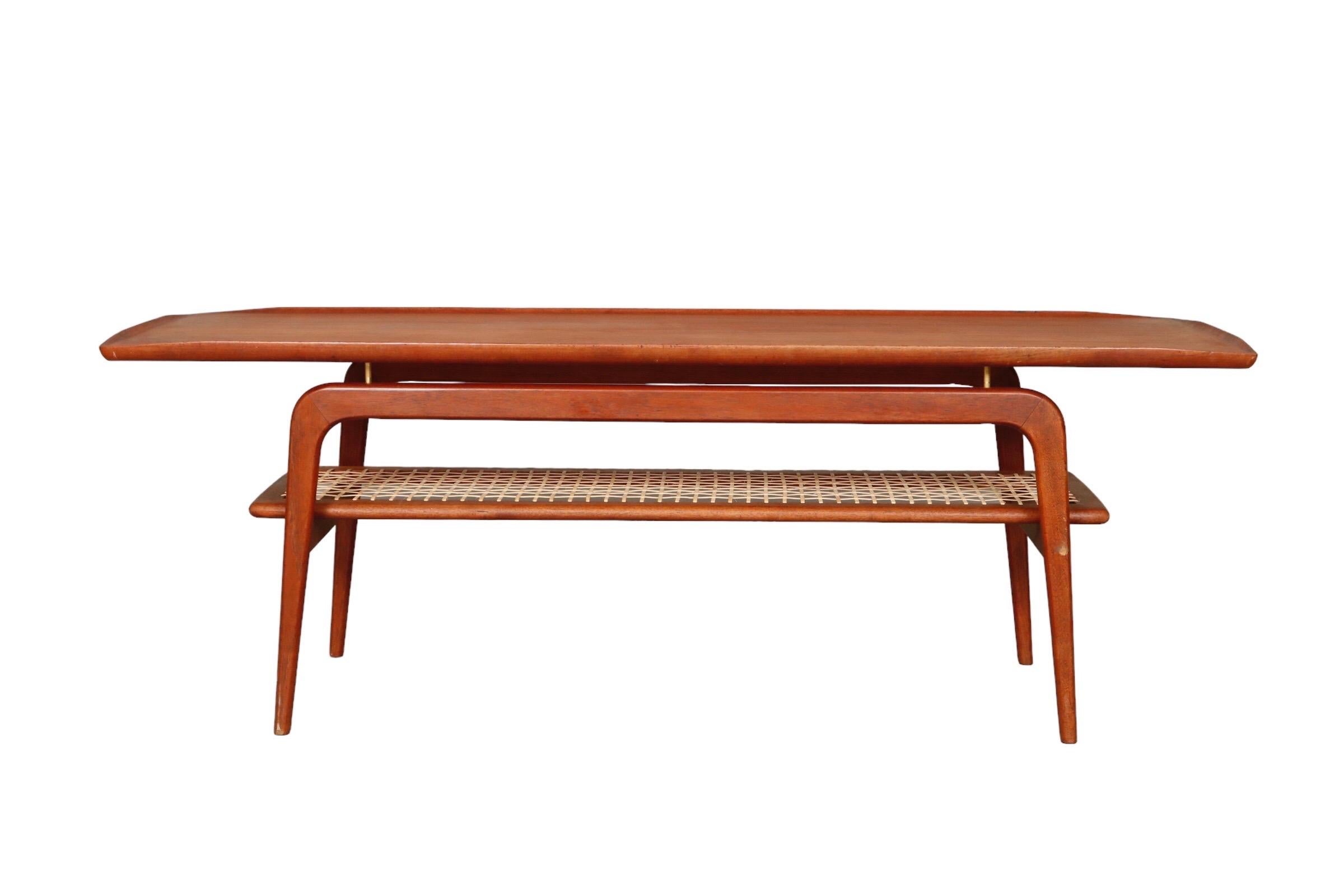 A 1960’s Danish mid century modern coffee table in teak by Arne Hovmand-Olsen. The table top floats over arched legs on fine brass supports. Below is a woven shelf inside a teak frame.

Dimensions: W58” x D20.5” x H21”.