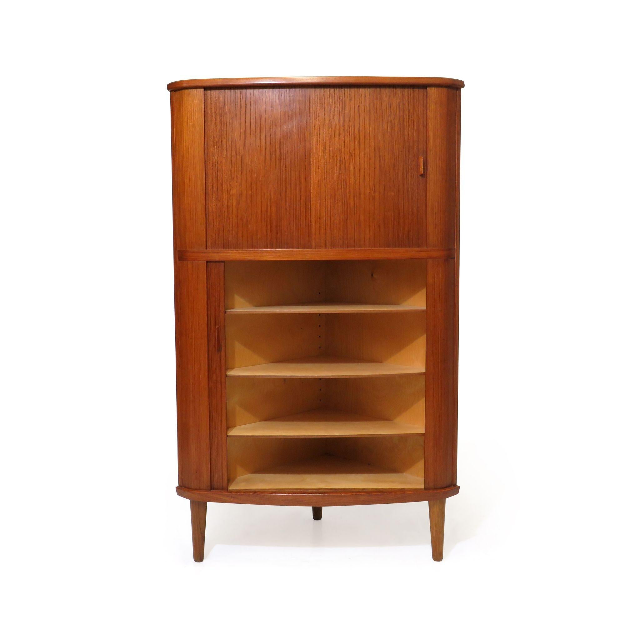 Mid-century Danish teak corner cabinet designed by Arne Hovmand Olsen for Skovmand & Andersen,1959, Denmark. The cabinet is crafted of teak with two sections of storage spaces with double tambour doors which open to reveal an interior of birch and