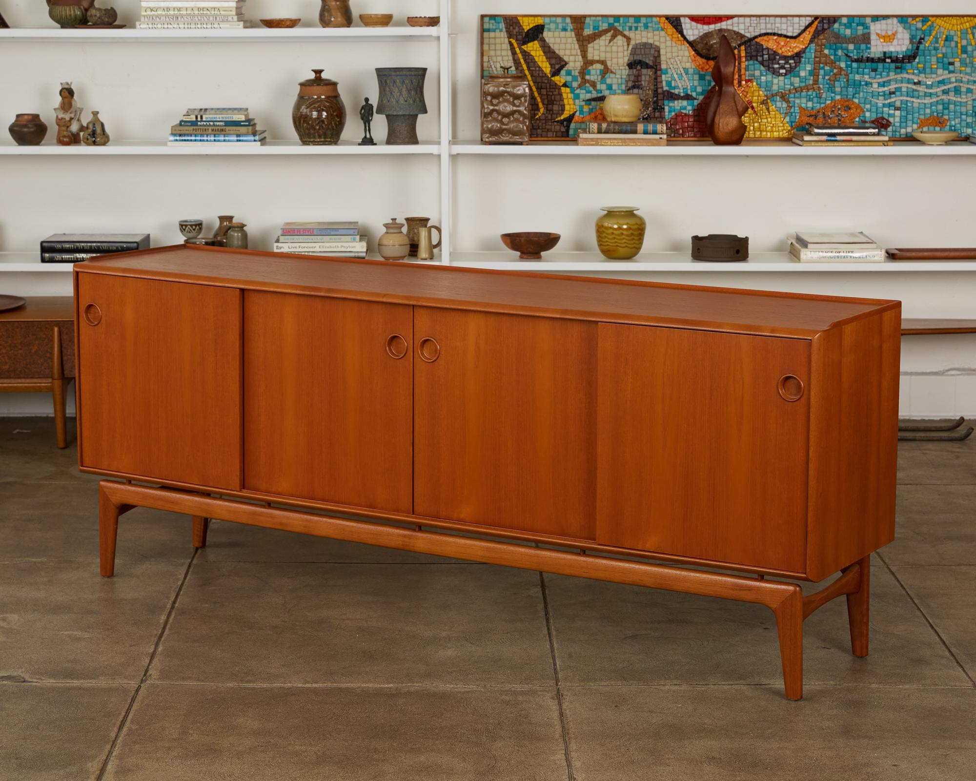 A Danish modern teak credenza or sideboard from Arne Hovmand Olsen for Mogens Kold Møbelfabrik. The piece has four sliding panel doors on two sets of runners, allowing flexibility of access or display. Each door opens at a recessed round pull. The