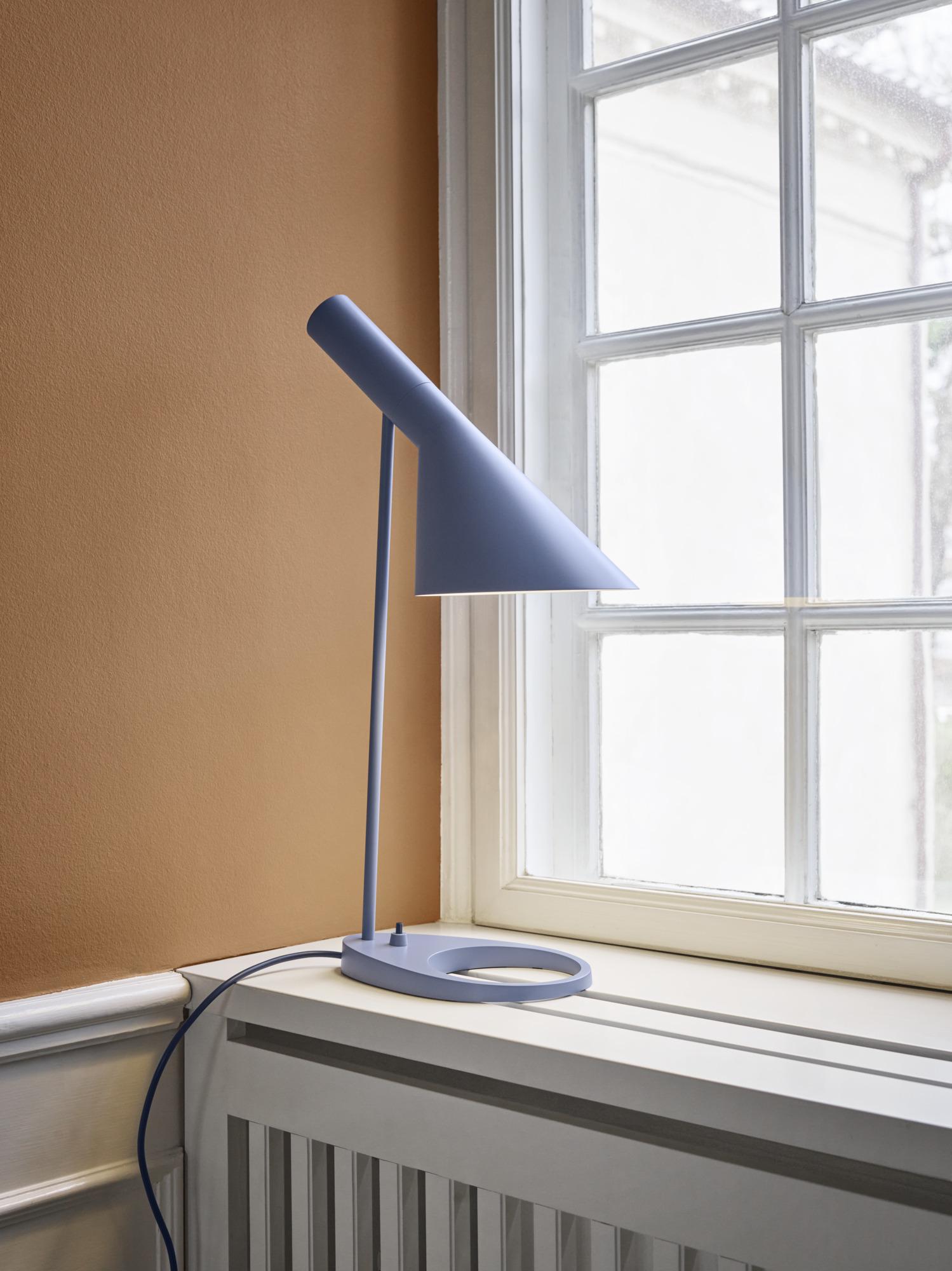 Lampe de table AJ d'Arne Jacobsen en bleu poussière pour Louis Poulsen. 

La série AJ faisait partie de la collection de luminaires que le célèbre designer danois Arne Jacobsen a créée pour le premier hôtel SAS Royal en 1957. Aujourd'hui, ses