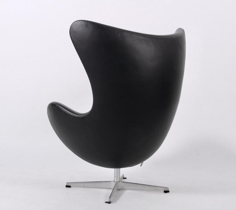 Egg lounge chair model 3316 and footstool model 3127 designed by Arne Jacobsen and produced by Fritz Hansen, made in Denmark. Original upholstery with beautiful anilline black leather. Tilt and return swivel functions. Original aluminum four-star