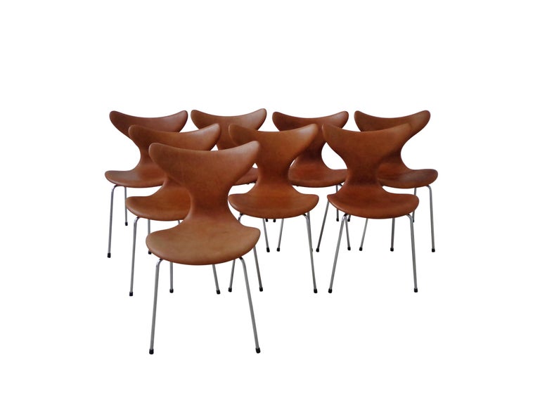A set of 8 dining chairs, model Lily 3108, designed by Arne Jacobsen in 1970, manufactured by Fritz Hansen. Arne Jacobsen first created the sleek, curvaceous Lily chair for Danmarks Nationalbank. The chairs are in great condition, the Cognac leather