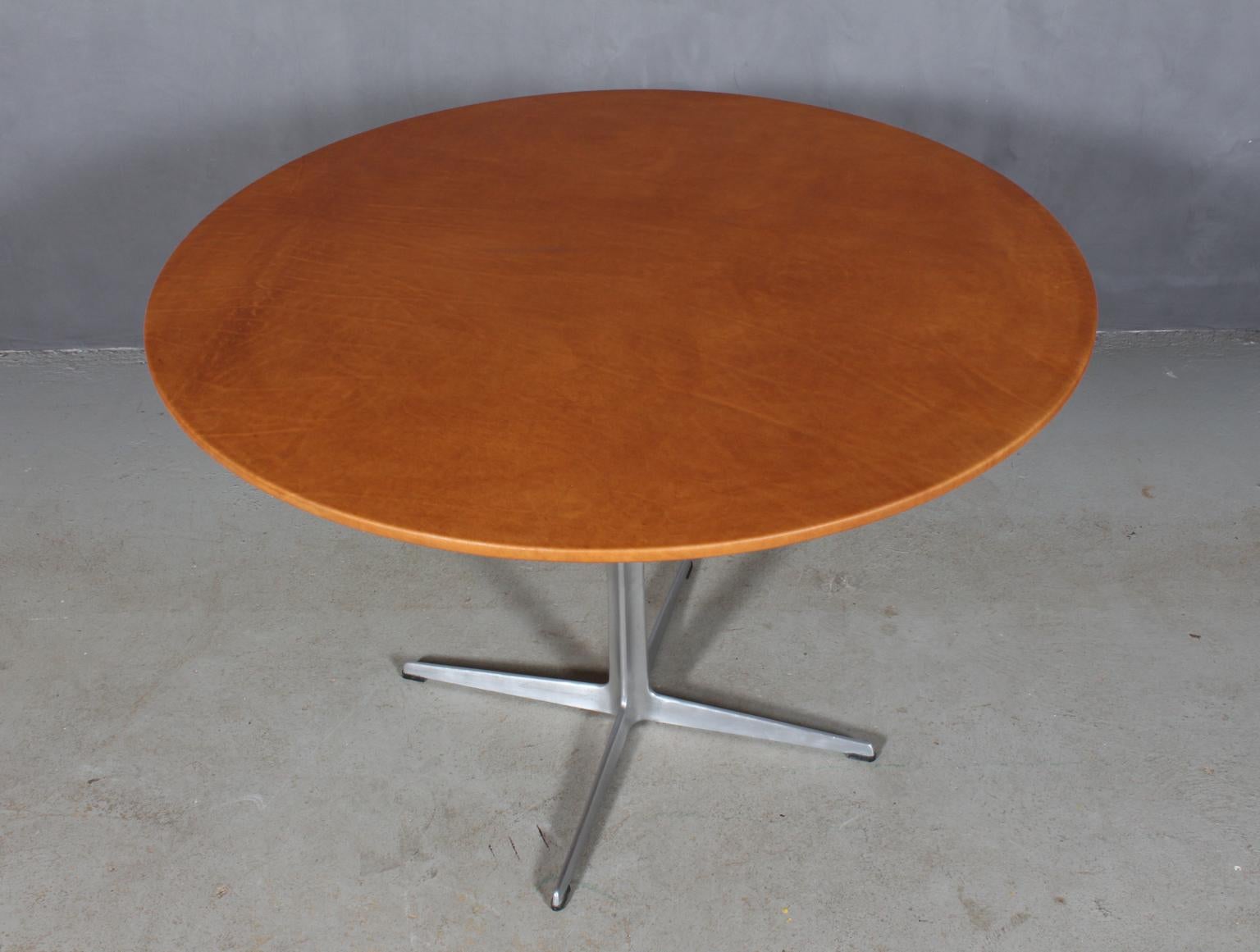 Arne Jacobsen round dining table with new upholstered plate with cognac Vintage aniline leather.

Four star profilated foot of aluminium.

Model 3513, made by Fritz Hansen.

The leather upholstery gives a unique and strong surface which will