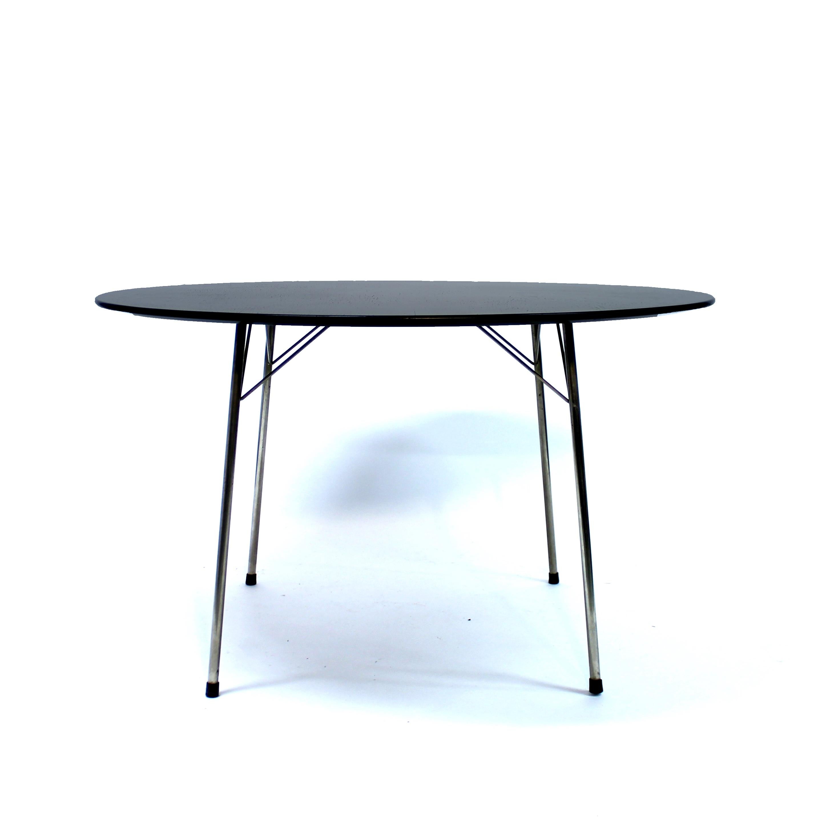 Circular dining table, model 3600, designed by Arne Jacobsen for Fritz Hansen. Black lacquered wooden table top with visable wood grain structure that sits on four chromed legs with black plastic 