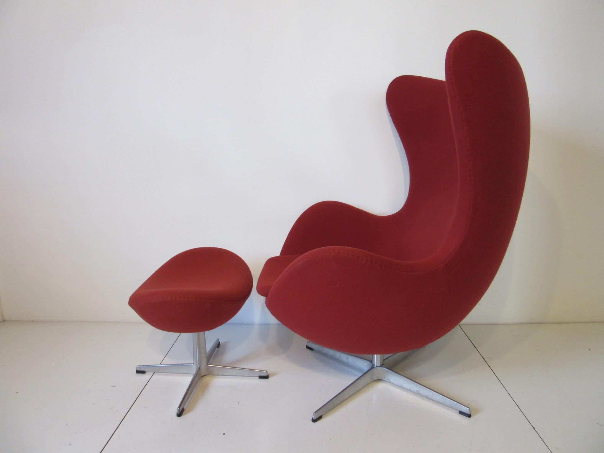 A swiveling and tilting Arne Jacobsen designed egg chair with matching ottoman in a darker red toned wool fabric, ordered with the optional adjustable tilting mechanism giving the chair added comfort. The ottoman size is 14.57