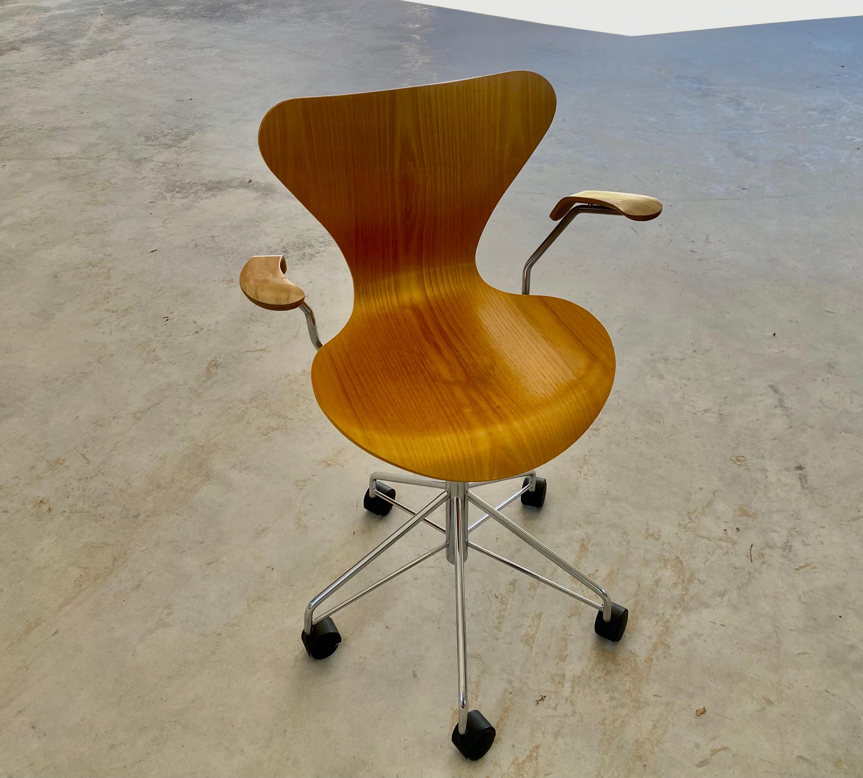Iconic Series 7 swivel desk chair, designed in 1952 by Arne Jacobsen for Fritz Hansen, this example dates 2000. The chair is clear waxed bent plywood, on a bright chrome base, with black plastic wheel coaster feet. In addition to being a swivel