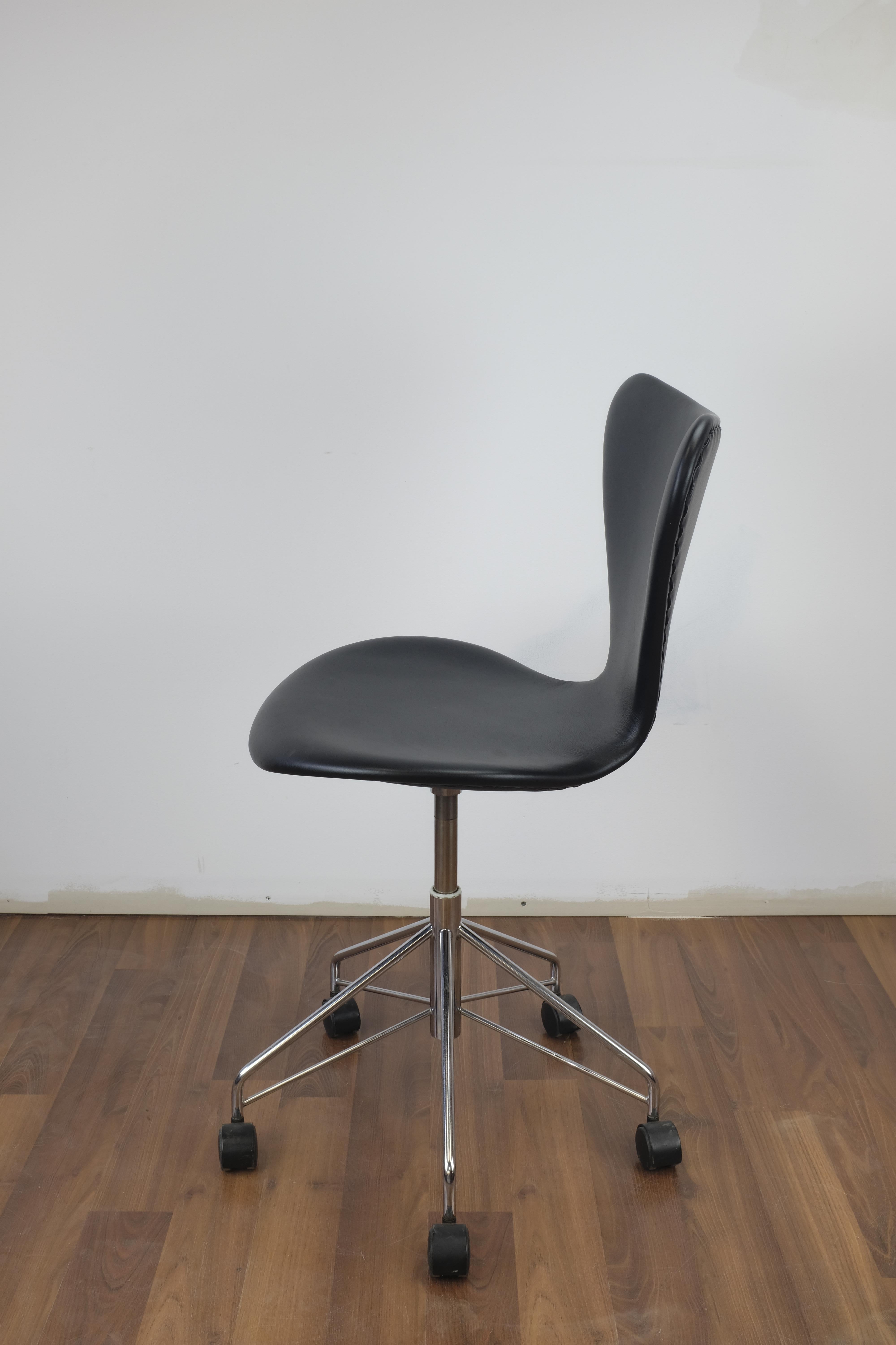 'Series 7' office chair designed by Arne Jacobsen in 1955. This example manufactured in Denmark by Fritz Hansen in 1997.

Seat is made of pressure molded veneer and has been reupholstered in black leather. The swivel base is made of chromed steel