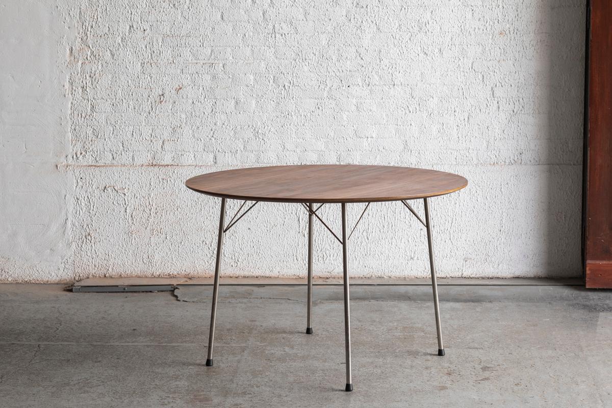 Round dining table ‘model 3600’ designed by Arne Jacobsen and produced by Fritz Hansen in Denmark in the 1950s. 
The Dutch brand Pastoe imported a number of designs by Jacobsen to sell them in the Netherlands. This is why there’s a small metal