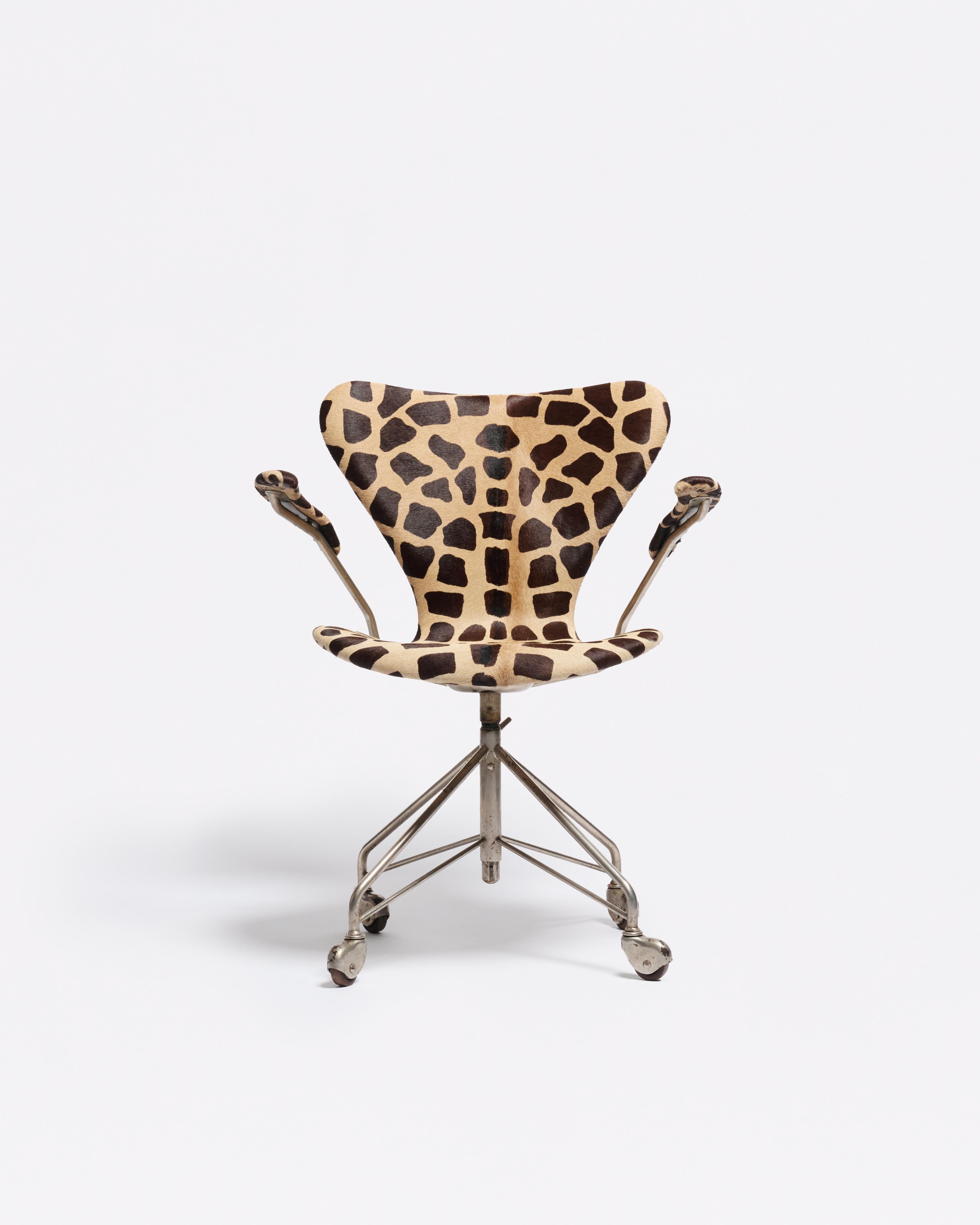 Une version inhabituelle de la chaise de bureau de la série 7 de Jacobsen, recouverte d'un tissu à motif de girafe et dont les pieds sont subtilement patinés. La forme reste immédiatement reconnaissable, mais la finition lui confère une présence