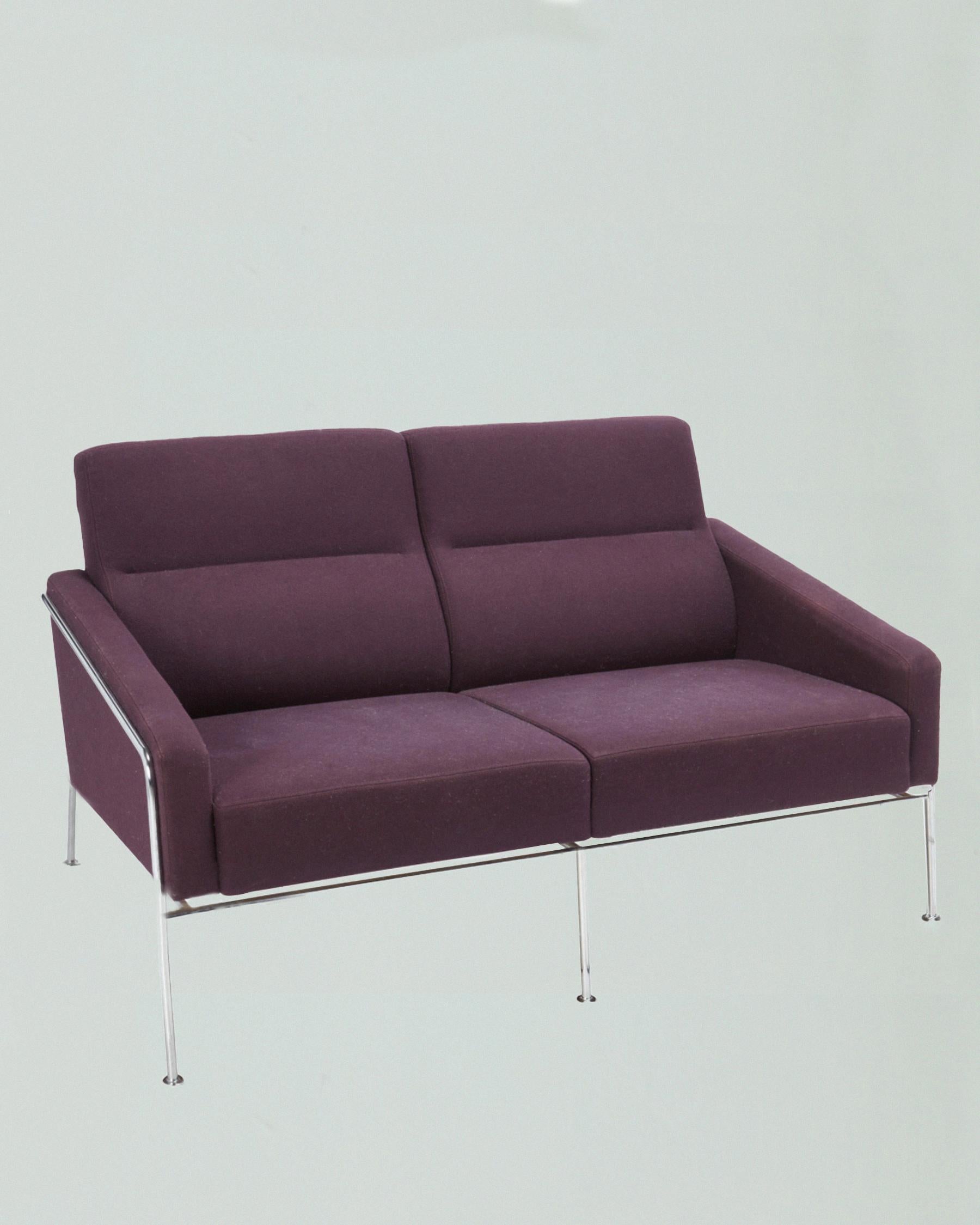 First designed in 1956, this sofa has a foil label to the underside: FH / Fritz Hansen / Made in Denmark. The two-seater sofa, upholstered in violet-colored wool, is in very good condition with its original fabric. The wrap-around chromed metal