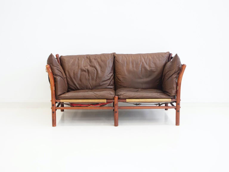 Two-seater sofa, model Ilona, designed by Arne Norell and manufactured by Norell Möbel AB. Dark stained beech frame, sides and back stretched with full-grain leather straps. One of the Loose cushions upholstered with brown leather.