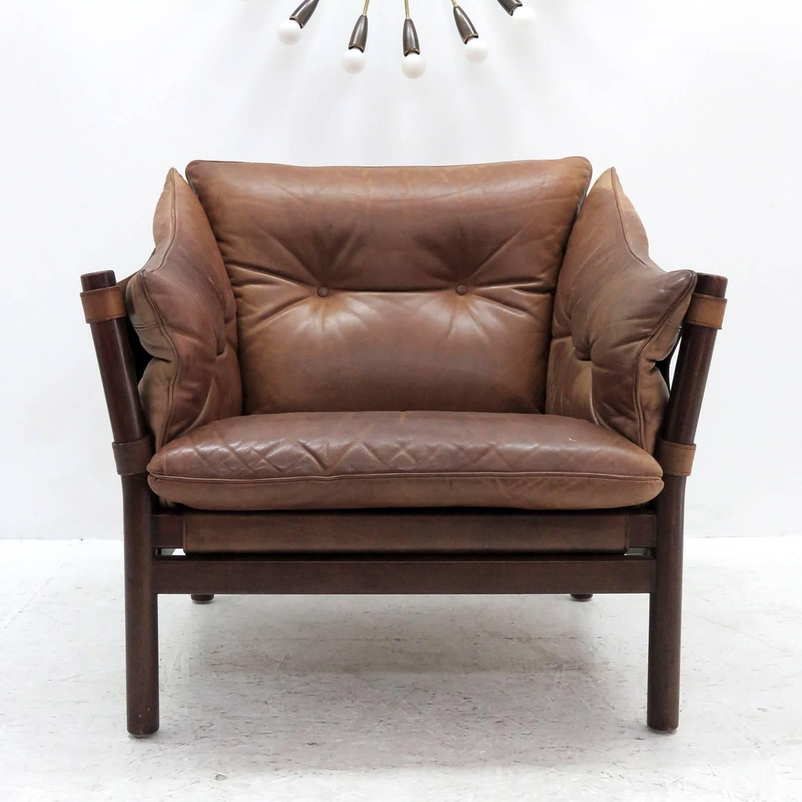 stunning pair of leather armchairs designed in the early 1960s designed and produced by Norell Möbel AB, Sweden, with thick tufted leather cushions on saddle leather sling supports with brass hardware, the frame is made of sturdy, dark stained solid