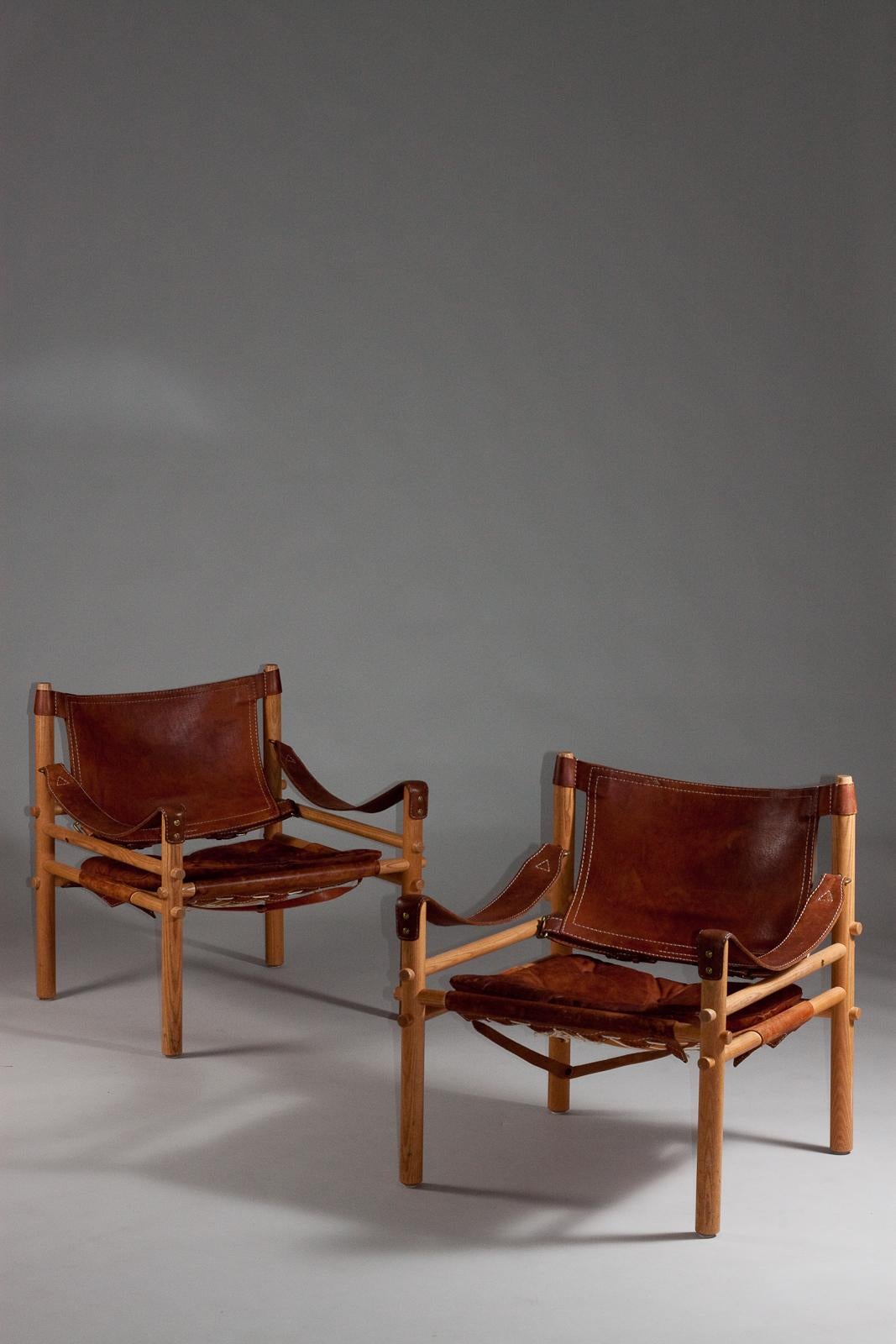 Add a touch of mid-century sophistication to your space with this stunning pair of 1960's Siroccio safari leather chairs by Arne Norell. Crafted in Sweden, these iconic chairs are known for their durable construction, comfortable design, and