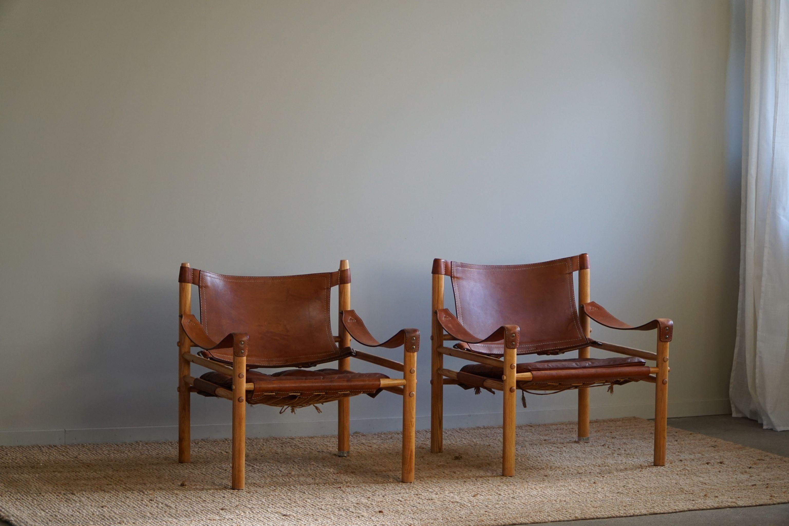 Beautiful pair of safari chairs in a warm red/brown leather and wooden ash frame. 
Designed by Arne Norell, produced by Arne Norell AB in Aneby, Sweden, in the 1960s.
This set is in a good vintage condition.

These appealing armchairs will fit into