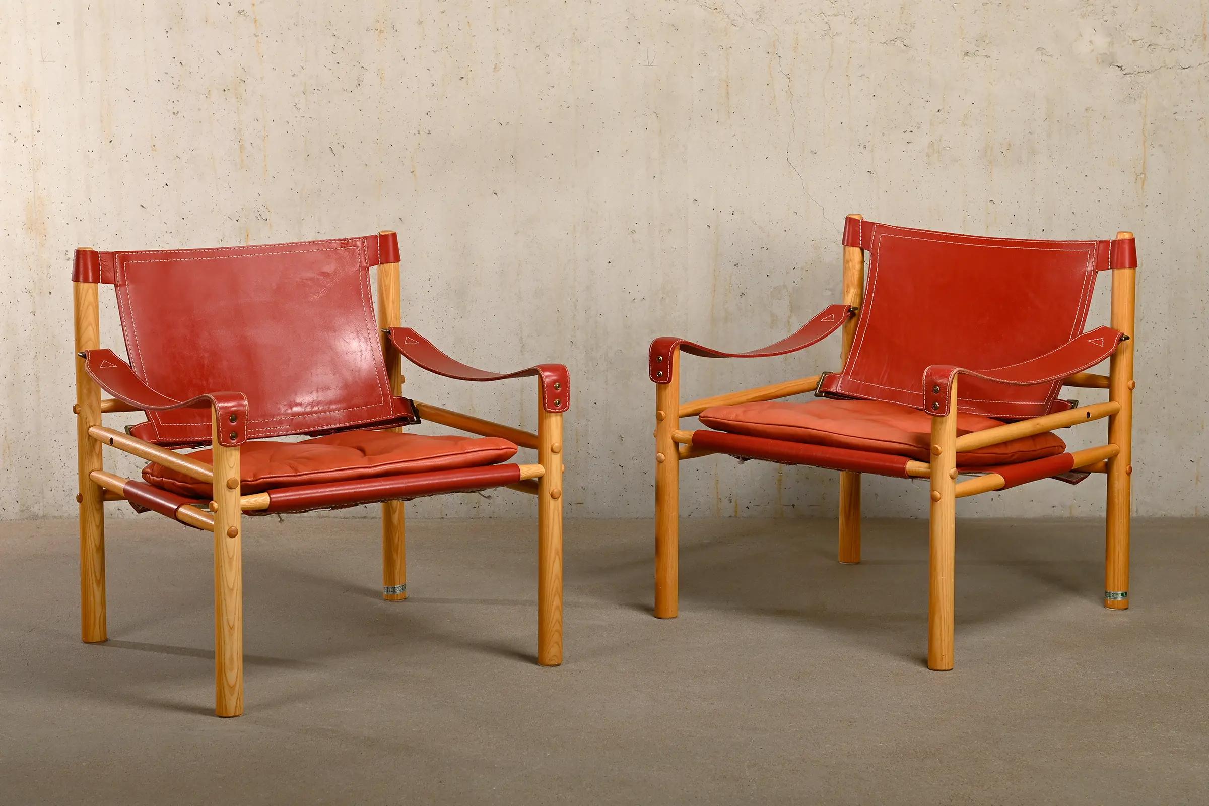 Tolles Paar Sirocco Safari Lounge Chairs, entworfen von Arne Norell und hergestellt von Norell Möbel AB in Schweden. Hell patinierte Eschenholzrahmen mit den originalen Lederkissen in schönem roten Leder. Alle in sehr gutem Zustand. Unterzeichnet