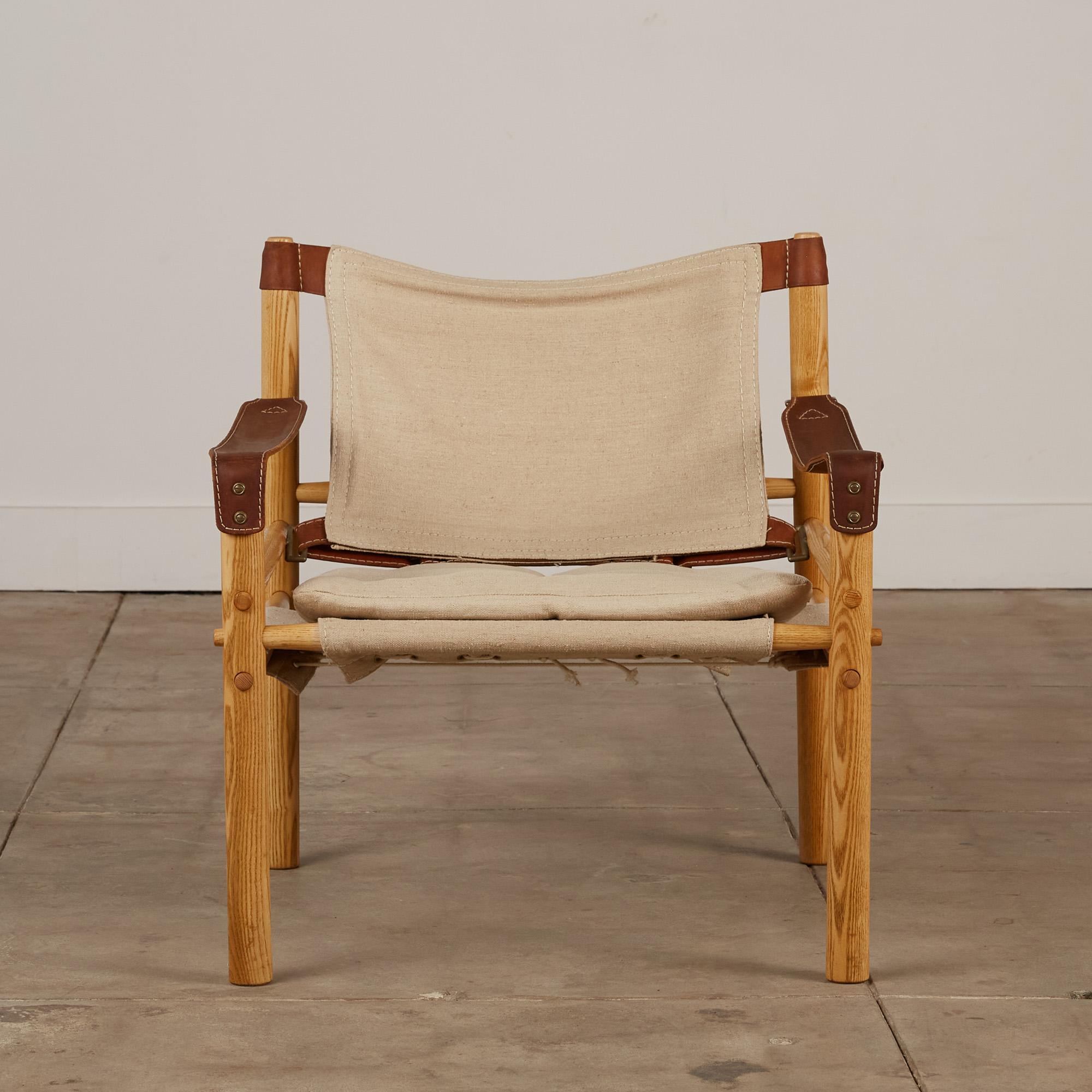 A safari chair designed by Arne Norell, made in Sweden c. 1960's. This chair features a solid oak frame strapped together by brown leather and natural colored canvas slings with brass fittings. A removable tufted canvas cushion sits on the lower