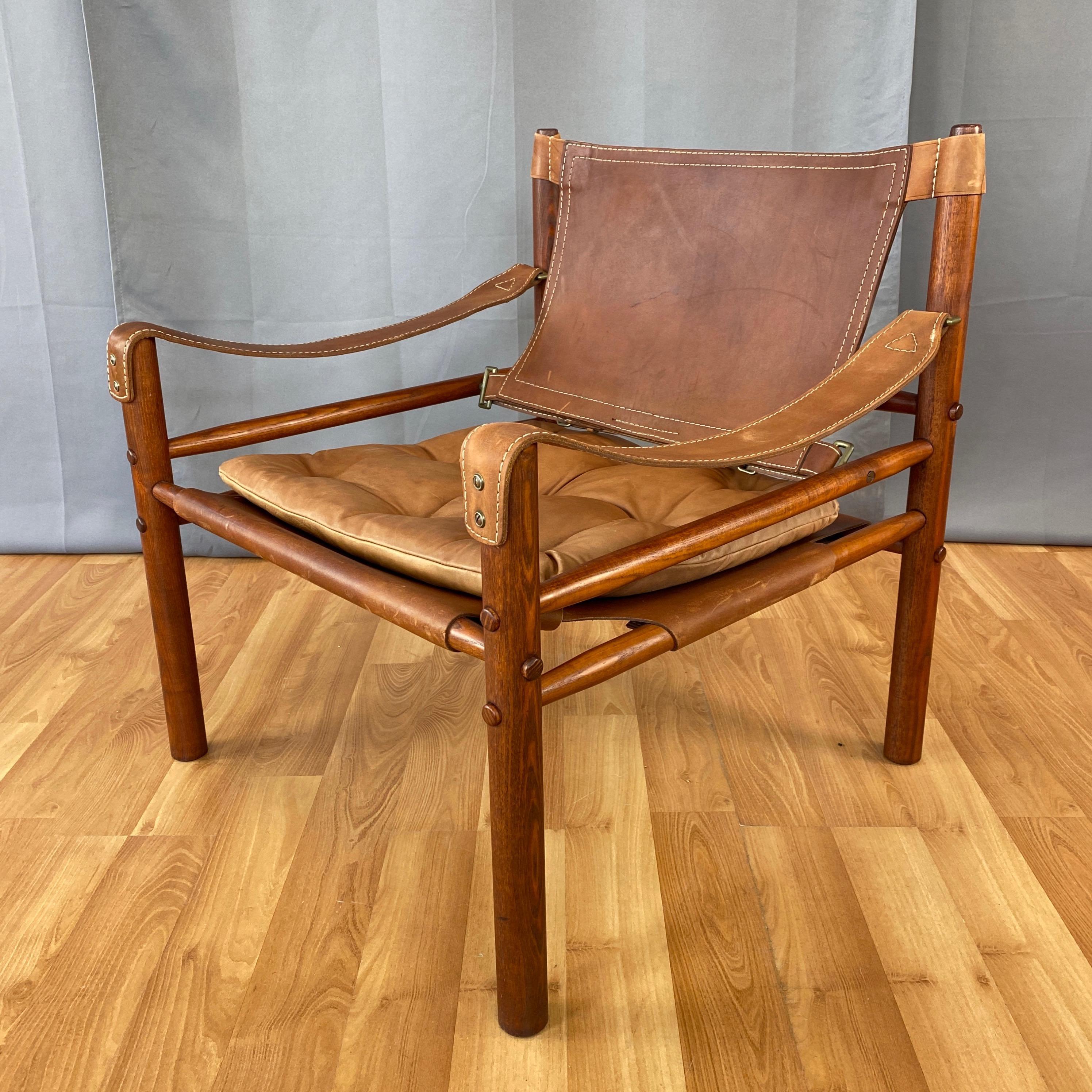 A very handsome 1970s Sirocco safari chair by Swedish designer Arne Norell in rosewood-colored oak and brown leather.

Solid oak frame with a tinted finish that gives it the appearance of vintage rosewood. Tapered dowel crosspiece elements fit