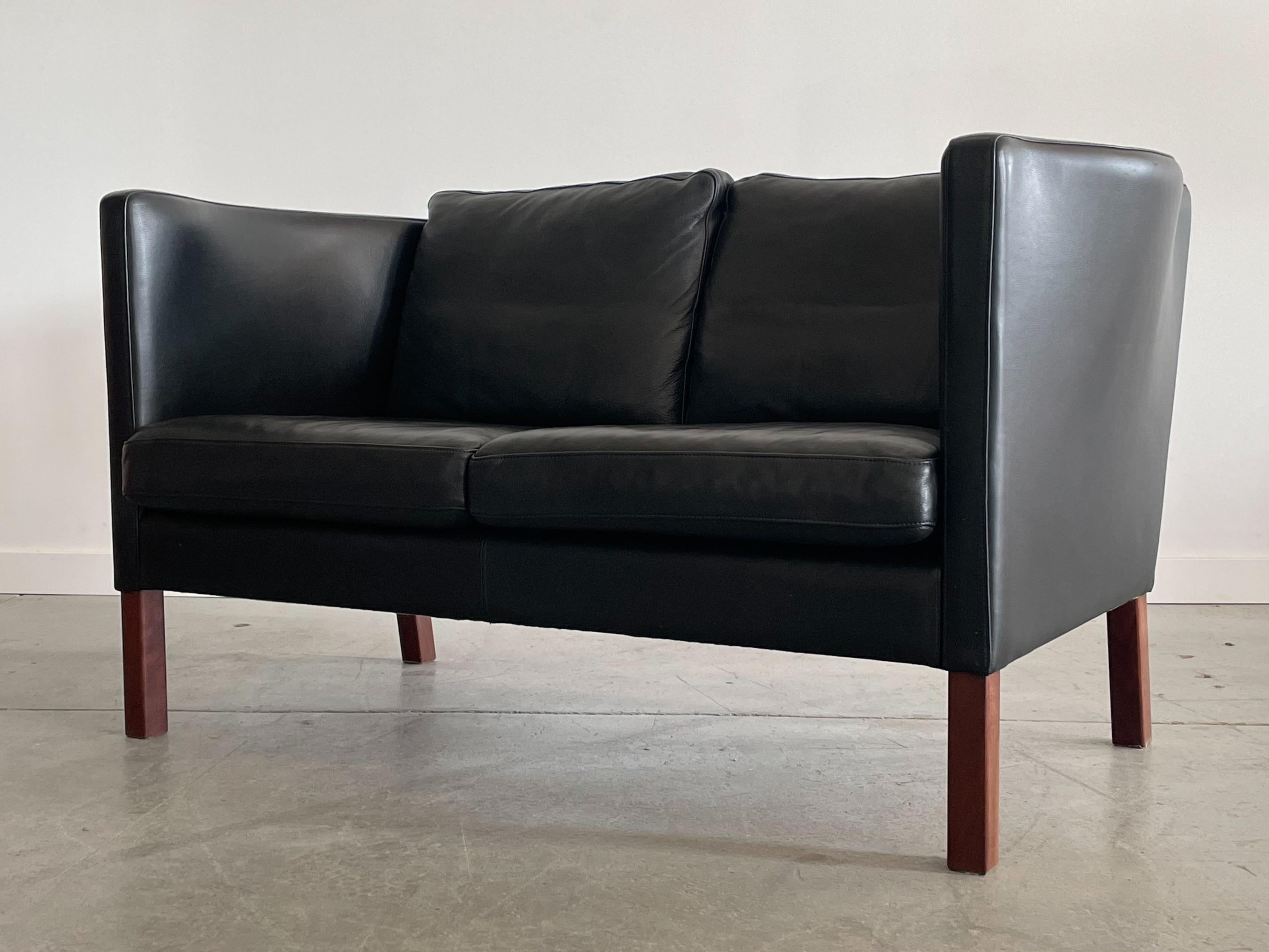Magnifique canapé deux places modèle AV59 conçu par Arne Vodder pour Nielaus, Danemark. Cette pièce présente un profil élancé typique des designs danois avec des pieds en hêtre teinté de bois de rose. Les panneaux latéraux profilés uniques offrent