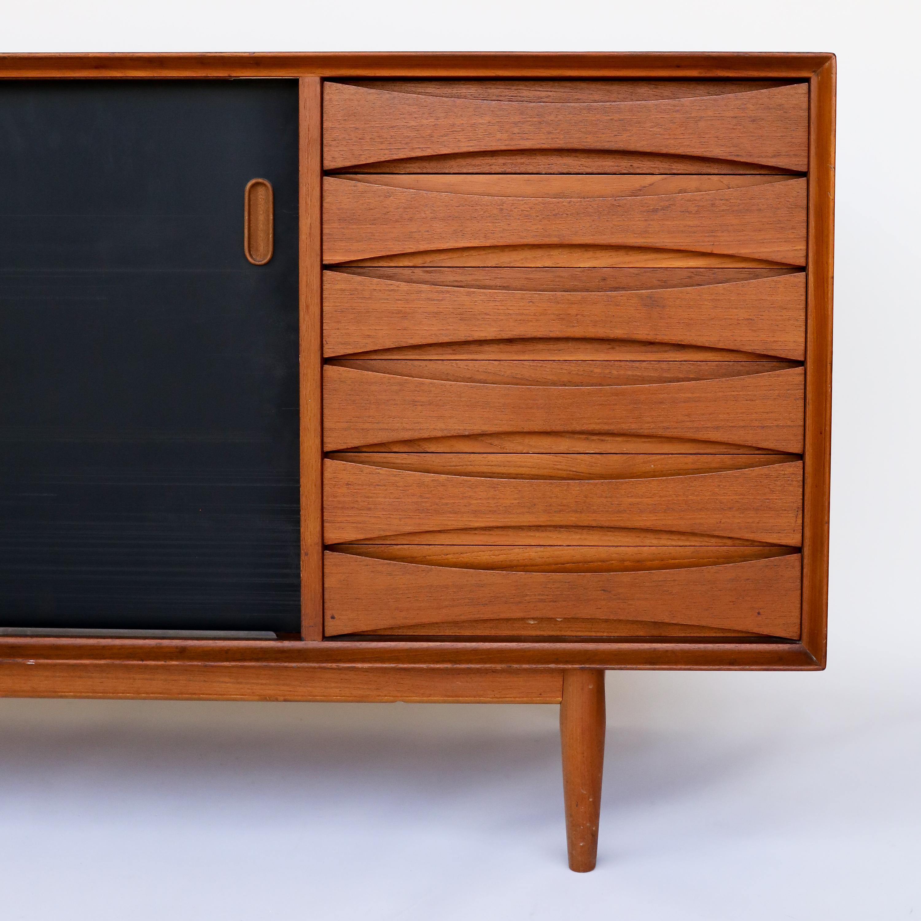 This is the iconic credenza Model 29, designed by Arne Vodder for Sibast. The doors are reversible with matte black lacquer on one side and teak on the other. 

The Model 29 sideboard has 6 drawers and 2 adjustable shelves behind 2 sliding doors.