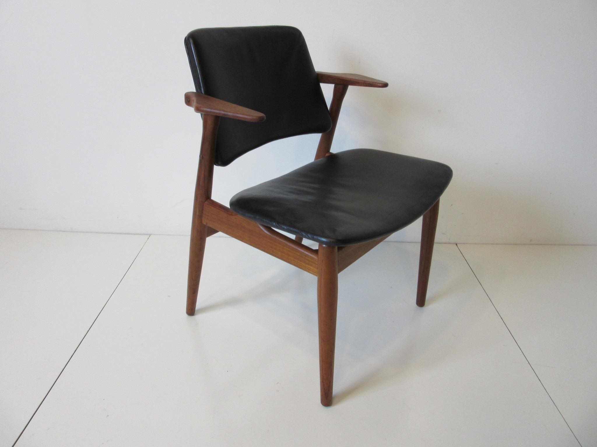 A dark teakwood chair with smaller upper arm rests and satin black leather seat and back rest still retains the original upholstery and manufactures branded mark. George Tanier Selections - Helge Sibast Made in Denmark makes a great living area or