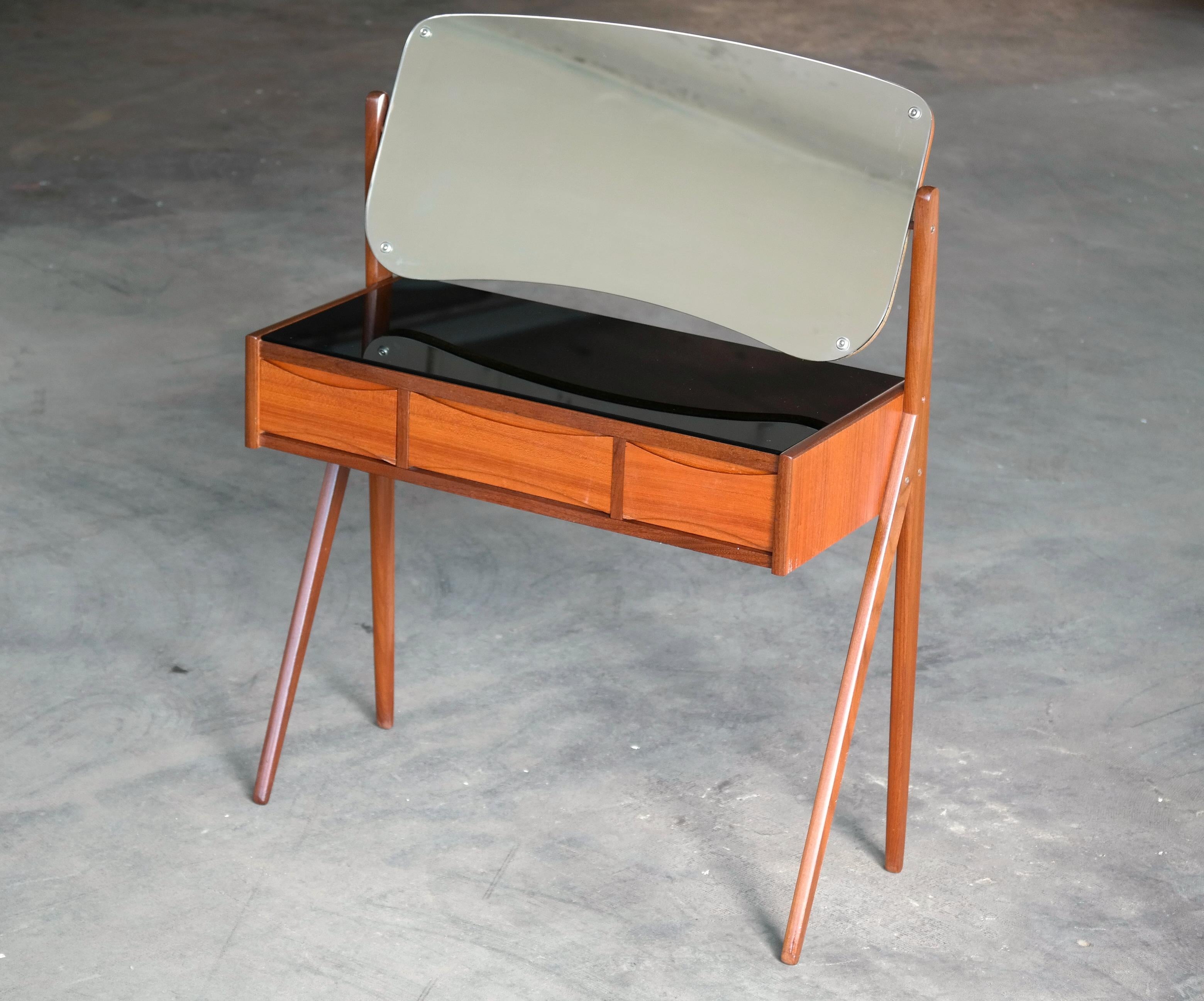 Very elegant vanity or small dressing table designed by Arne Vodder in Denmark in the 1960s. Cabinet made from dark teak and the drawer fronts in light colored teak veneers creating a nice two-tone - topped with a black glass top over three drawers