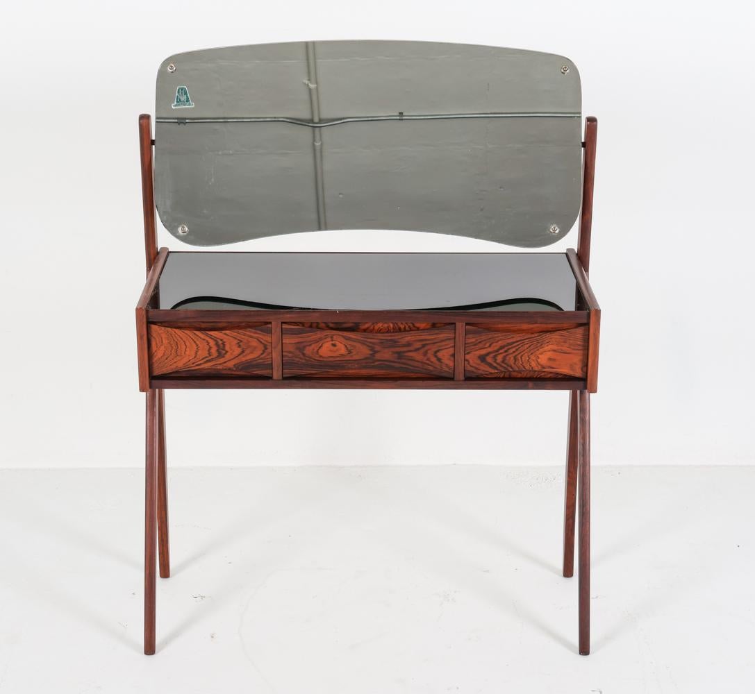 This attractive little dressing table was designed by Arne Vodder, an iconic Danish designer known for his mid century creations. This vanity was produced by Olholm Mobelfabrik sometime in the 1960's. It has been constructed with rosewood veneer, as