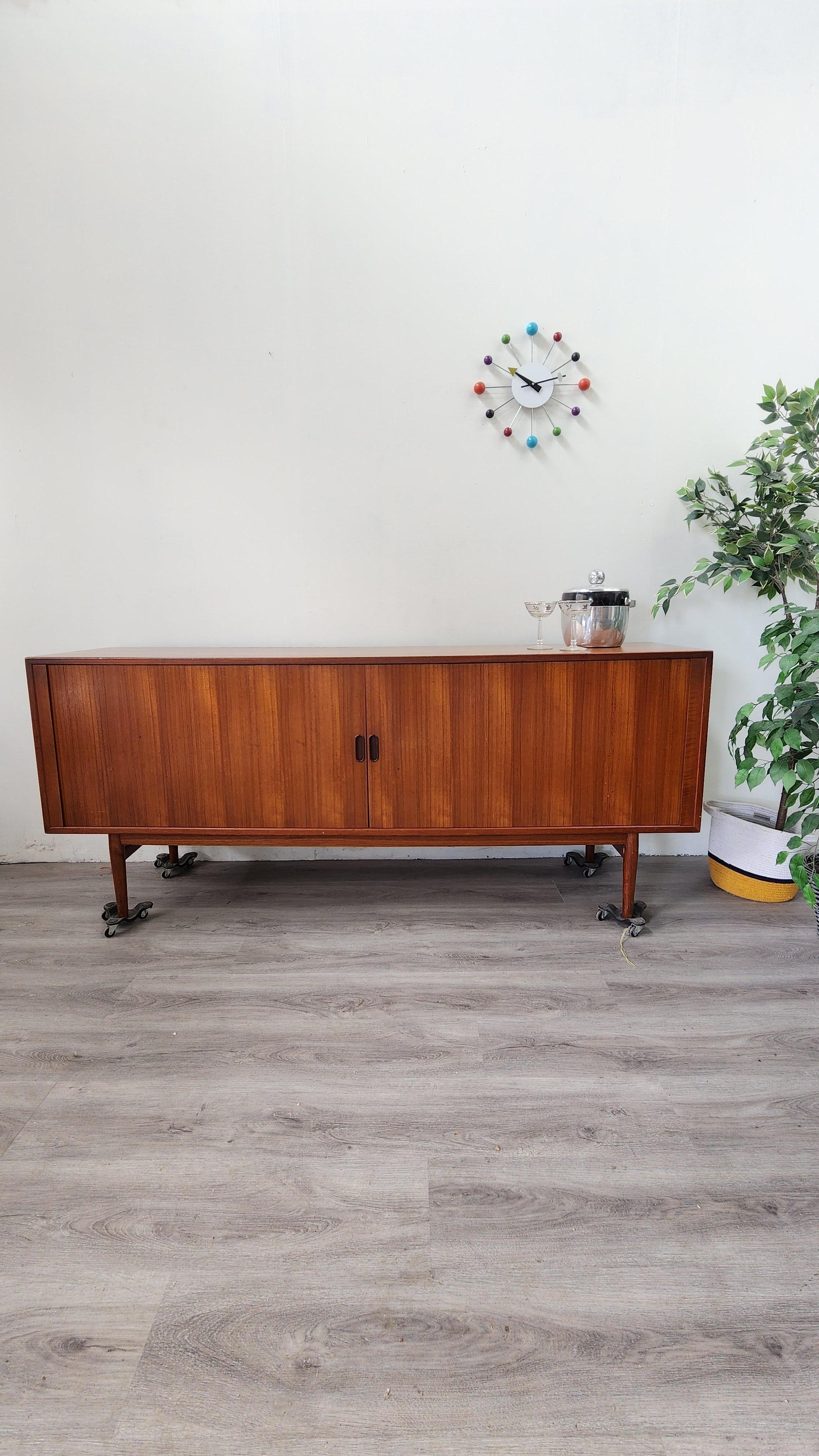 This beautiful teak credenza was designed by famed Danish designer Arne Vodder for Sibast Mobelfabrik. The tamboured doors were psinstcraftedv with perfectly matched veneer that slide away beautifully. 
Behind the tamboured doors is plenty of