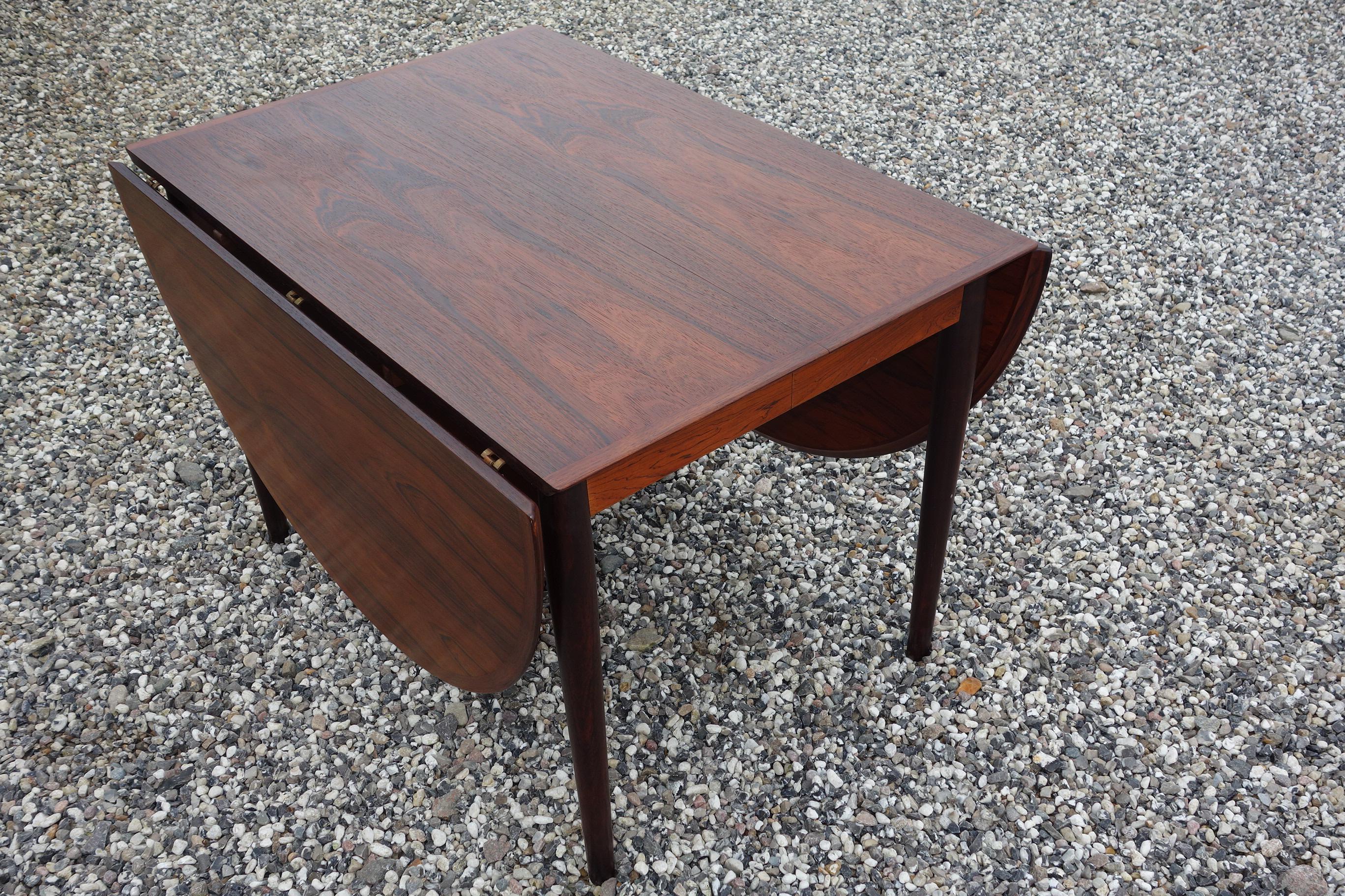 Arne Vodder. Dining table made of veneered rosewood with extension, fitted with semi-circular flaps on each side, 1 additional plate with sash included. Round tapered legs. Produced by Sibast Furniture, model 227. Measures: H. 72 cm., B. 106 cm., L.