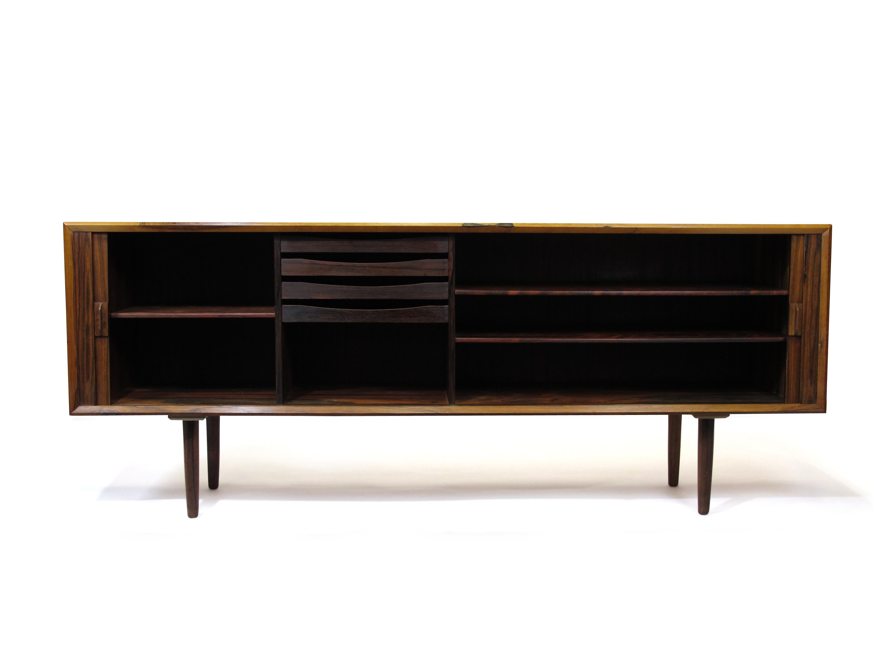 Rosewood credenza designed by Arne Vodder for Sibast, Denmark circa 1961. Features a book-matched tambour door front, which opens to reveal a series of adjustable shelves and silverware drawers. Raised on round tapered legs and has a finished back.