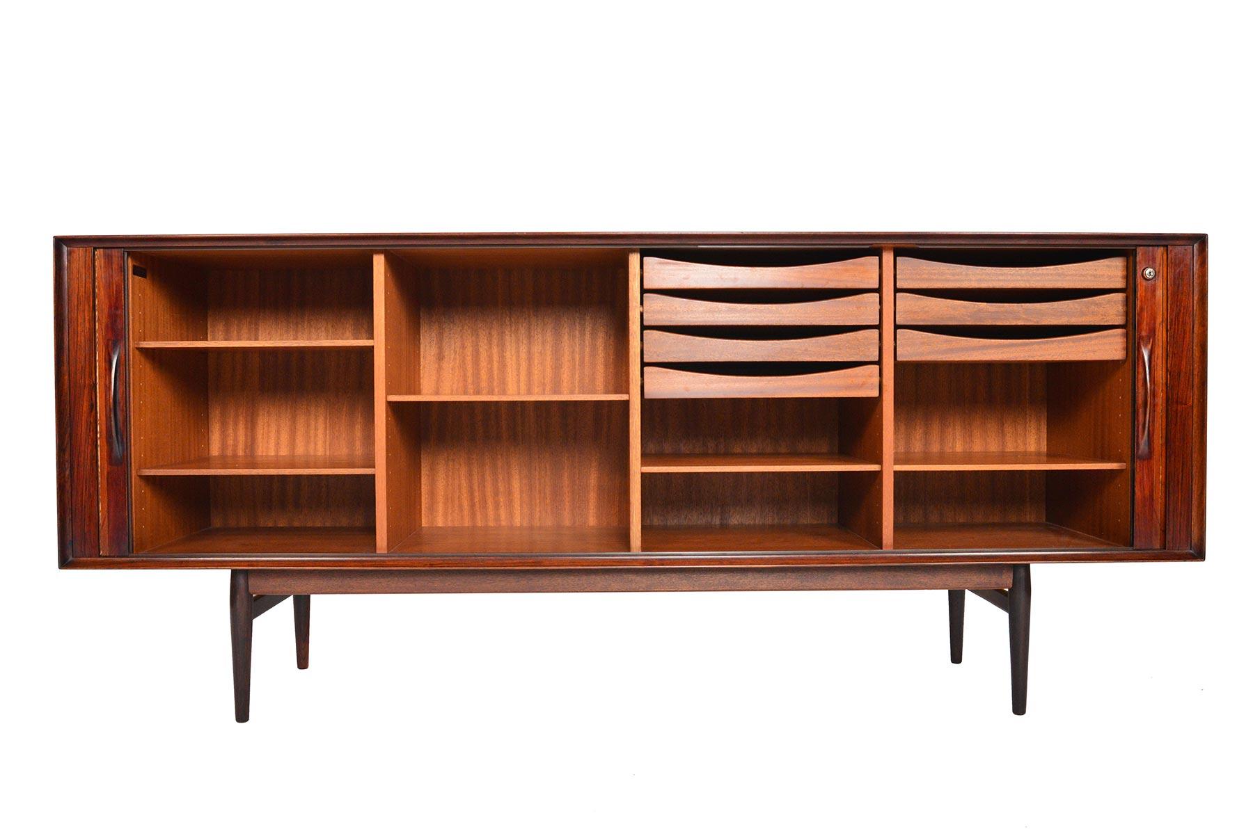 This Danish modern large Brazilian rosewood tambour door credenza was designed by Arne Vodder for Sibast and features a sleek profile and ample storage! The smooth running tambour doors open to reveal four bays outfitted with seven drawers and five