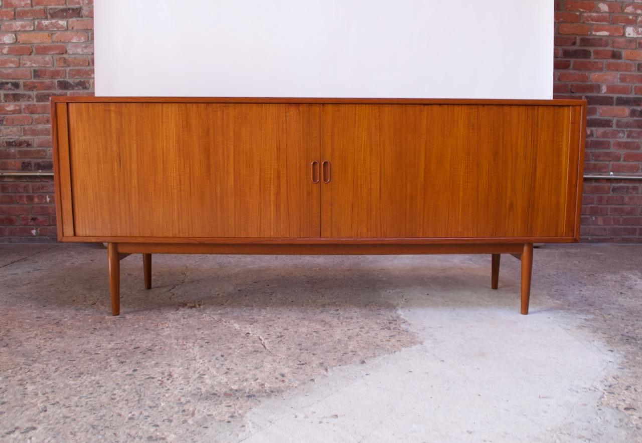 1950s Danish modern teak credenza (model 37) designed by Arne Vodder for Sibast Møbler. Composed of a teak frame with two tambour doors with recessed pulls that slide open to reveal a total of four adjustable shelves (three shorter on the right side