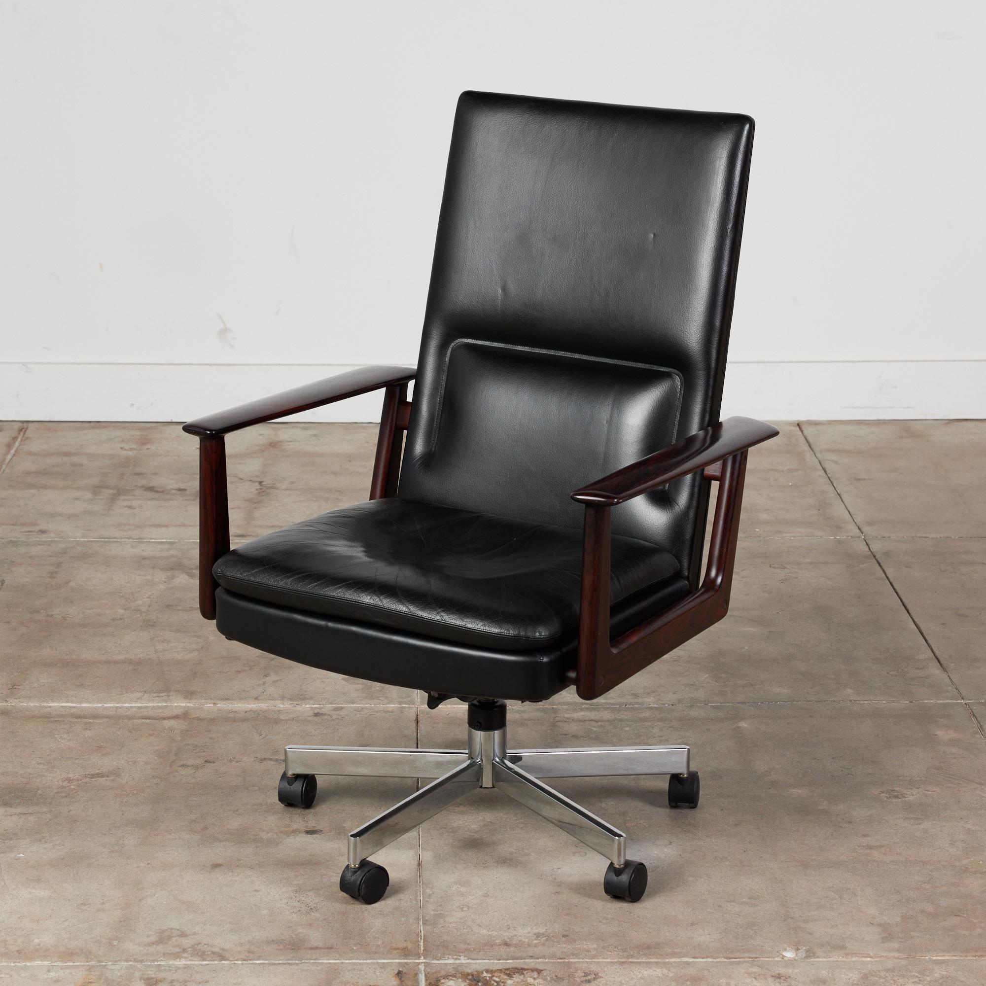 Desk chair by Arne Vodder for Sibast, c.1960s, Denmark. The armchair features black leather upholstered seat and tall seatback. The armrests are a beautiful dark rosewood The chair height is adjustable and sits on a chrome metal base with five