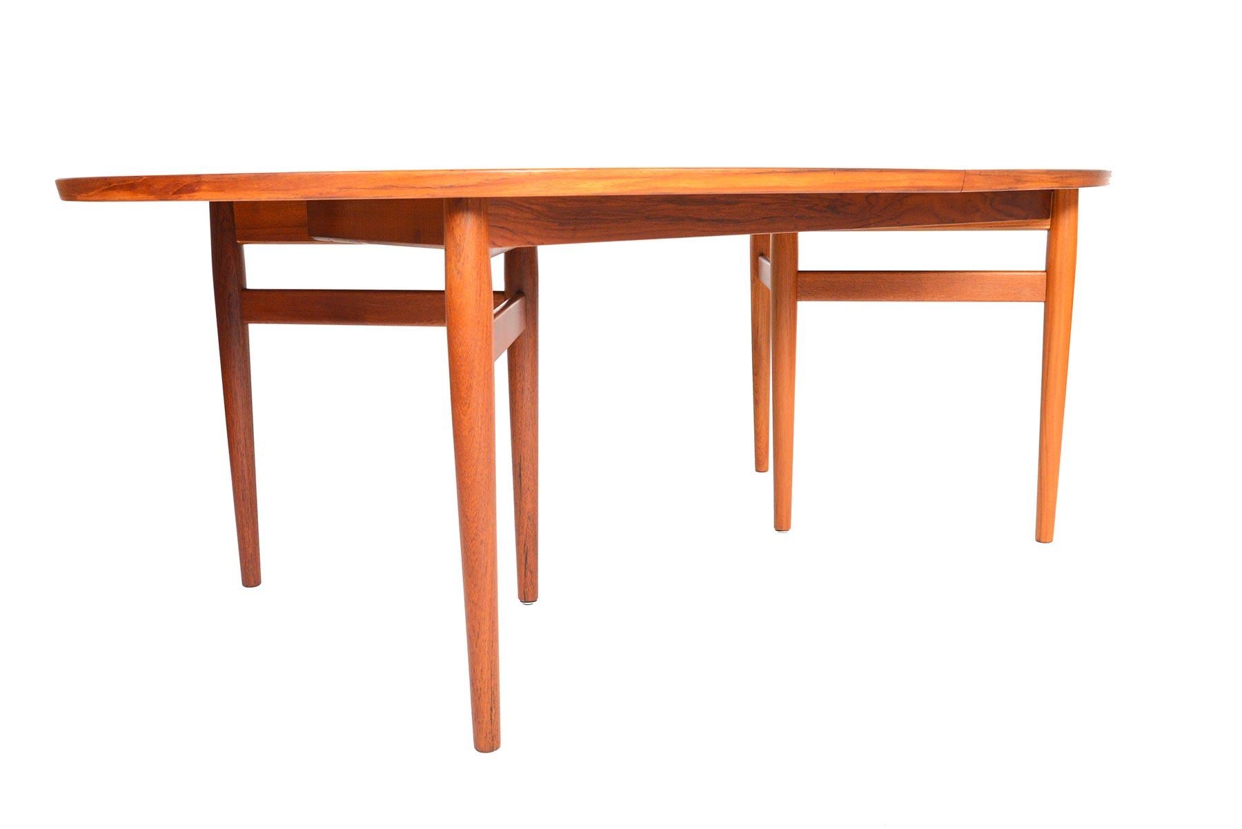 This stunning Danish modern Model 212 oval dining table in teak was designed by Arne Vodder for Sibast in the 1960s. Flush banding and deep- set apron create a sleek and spacious form. Each table half stands on a braced three leg base. Center legs