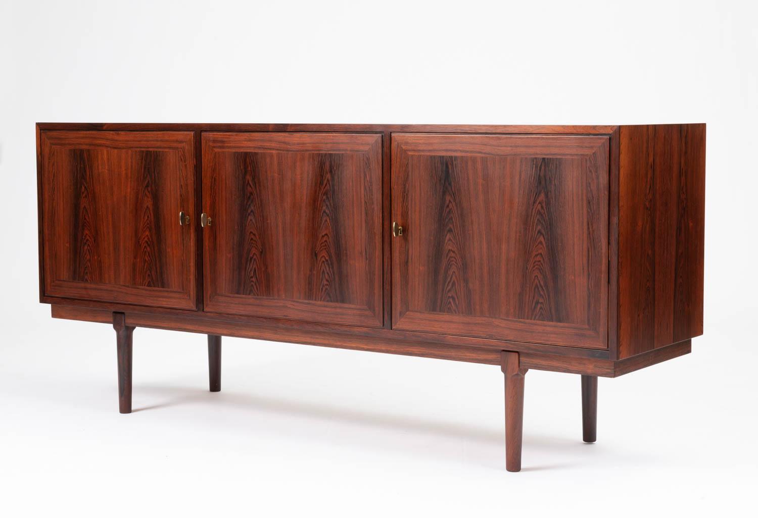 A striking rosewood credenza by Arne Vodder for Vamo Sonderborg. The credenza features three hinged rosewood doors with beautiful grain that open and can be locked by individual brass keys. The two outer sections each feature a single adjustable