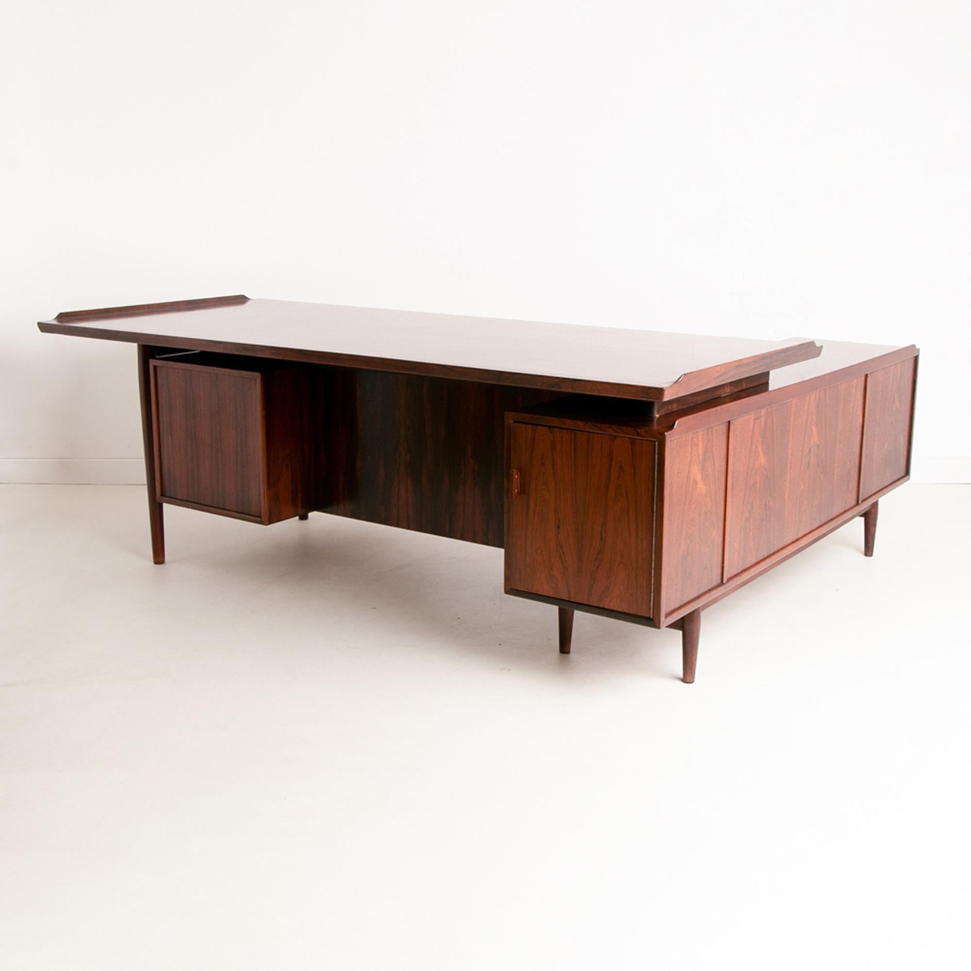 A Danish midcentury rosewood corner desk designed by Arne Vodder for Sibast Mobler. The desk features a sideboard to the left of the desk adding extra storage and surface space.
