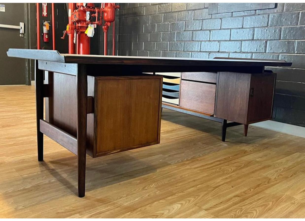 Danish modern executive desk by Arne Vodder for Sibast made of Rosewood, circa 1960s. The main desk features two drawers (tray & file storage) and on the back, a compartment with two shelves. The return desk features a sliding door with shelves, 5
