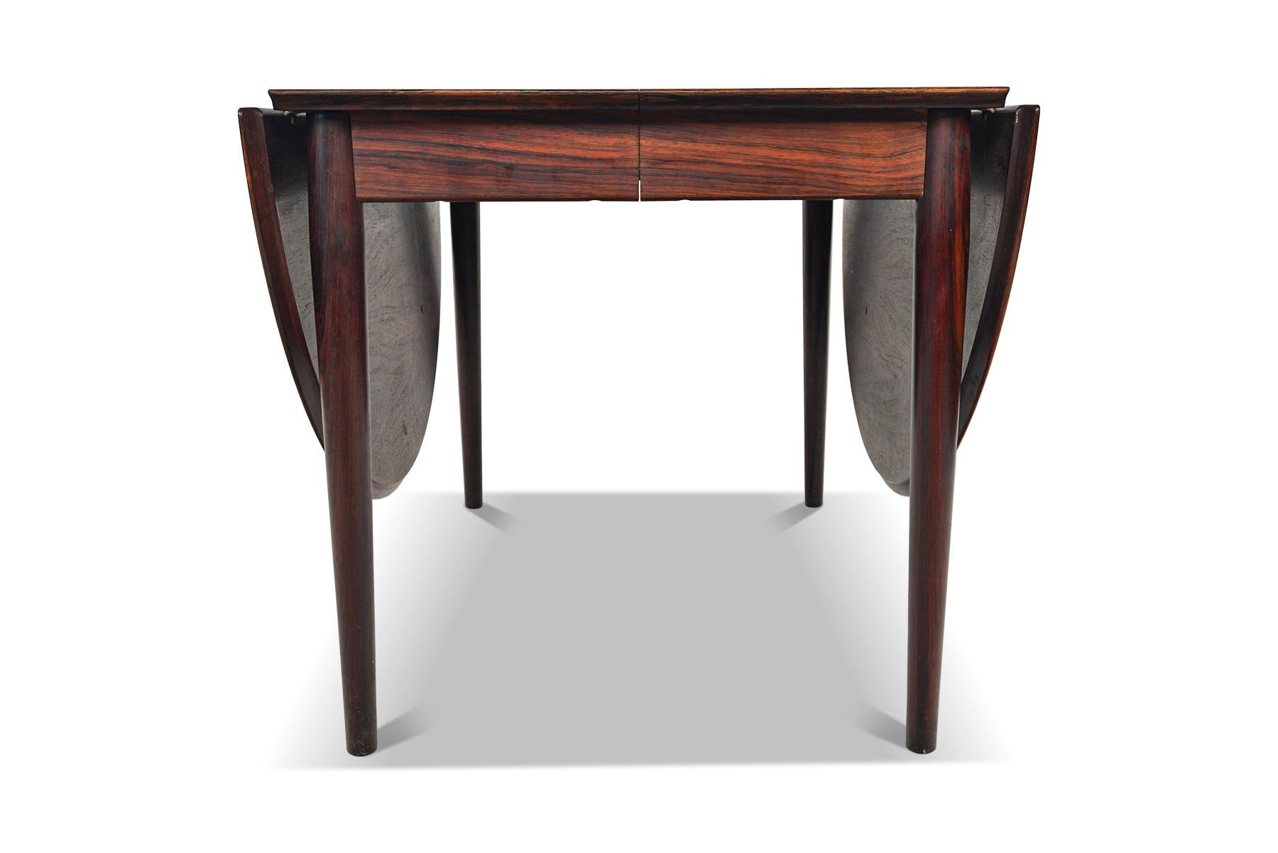 This stunning Danish modern dining table was designed by Arne Vodder in the 1950s. This table features two drop leaves on the exterior and opens to hold two additional skirted leaves. This table can comfortably seat four to ten guests. In excellent