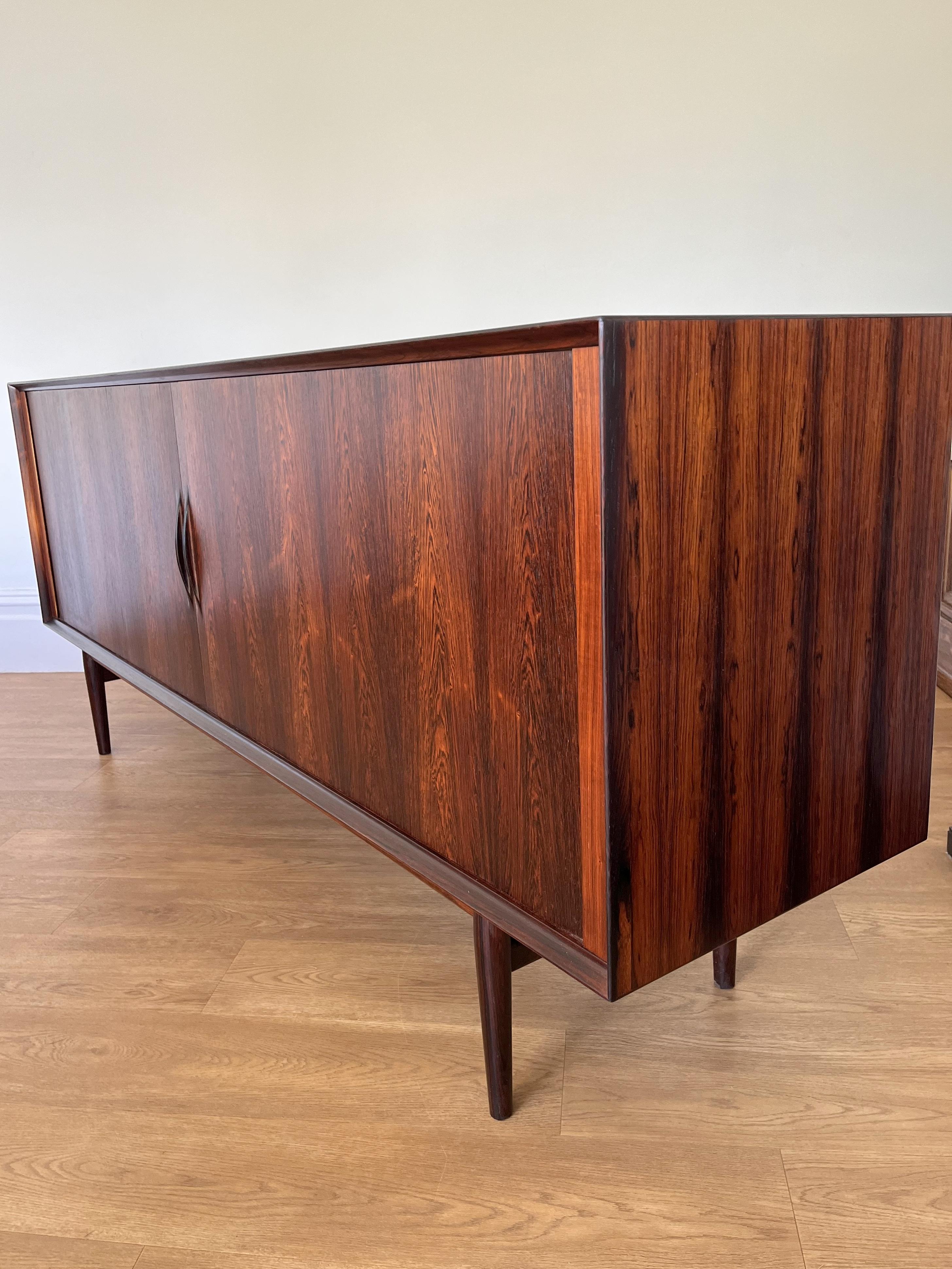 Rosewood veneered, sideboard designed by Arne Vodder for Sibast, Denmark.

The sideboard features sliding tambour doors with beautifully crafted carved handles and sits on 4 solid rosewood turned legs.

The interior has 3 draws and four
