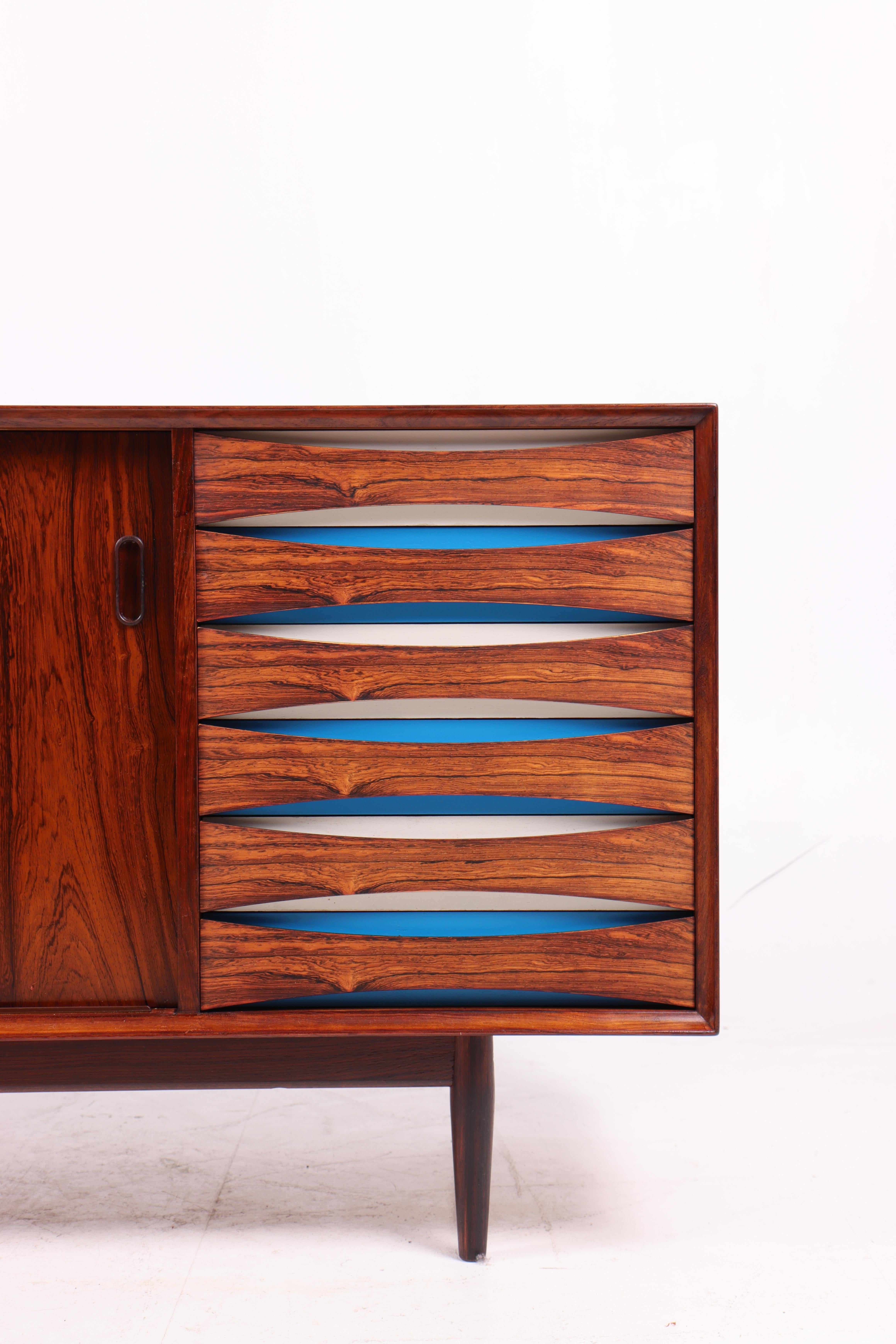 Aparador elegante y distintivo diseñado por Arne Vodder en los años 50 y fabricado por Sibast Møbler en Dinamarca. Fabricada en palisandro con vetas bellamente labradas, la pieza presenta dos puertas correderas y una fila de cajones en colores