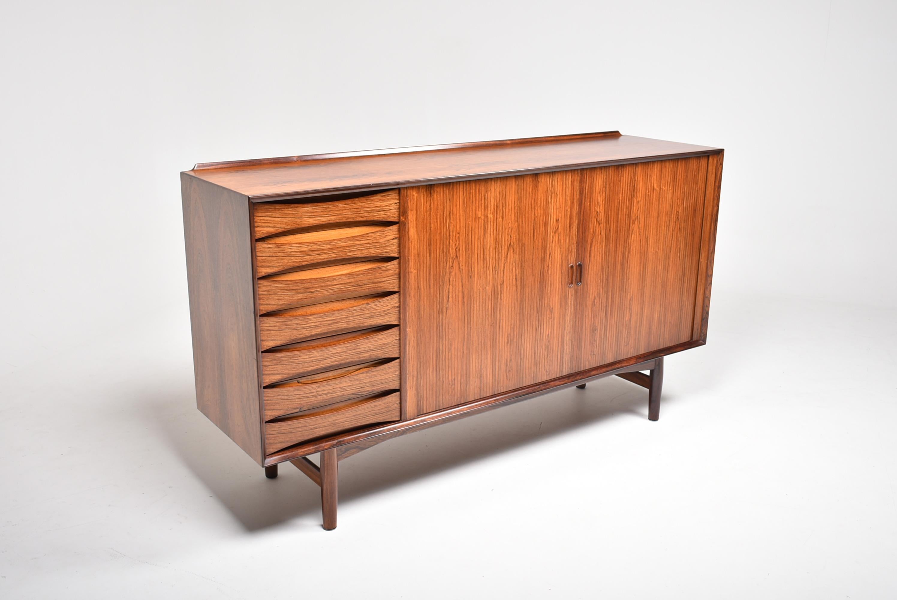 Refined sideboard in rosewood, designed by Arne Vodder for the danish cabinetmaker Sibast.
On the back of the top is a discreet winglet, to avoid any object falling.
On the left we have seven drawers with concave edge pulls (in France this part