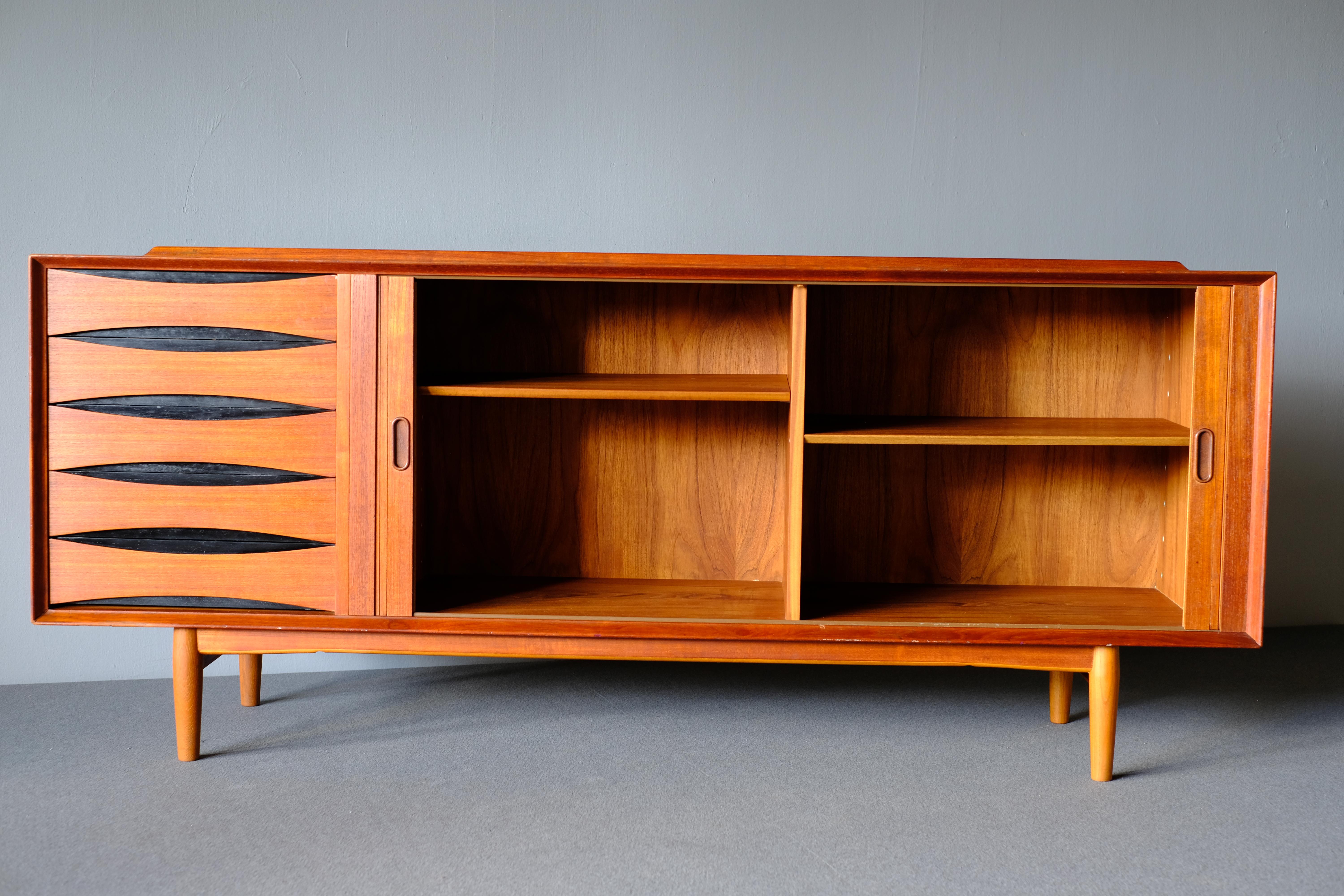 Arne Vodder sideboard in teak for Sibast Furniture. This wonderfully designed piece has 2 ingenious tambour doors which open to reveal shelving. It has 5 drawers with Vodder’s signature distinctive drawer pulls with black lacquered back panels. A