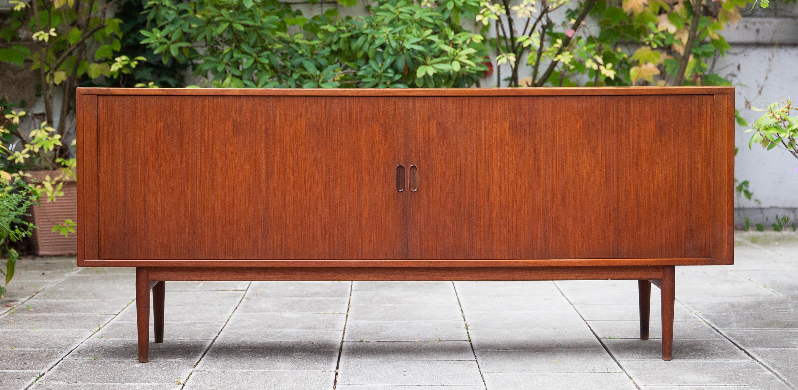 Scandinavian modern sideboard designed by Arne Vodder for Sibast.
Richly grained teak. Sideboard has tambour doors and shelves and 2 drawers behind. The inside of the sideboard is complete, nothing missing. This sideboard is finished all over so it