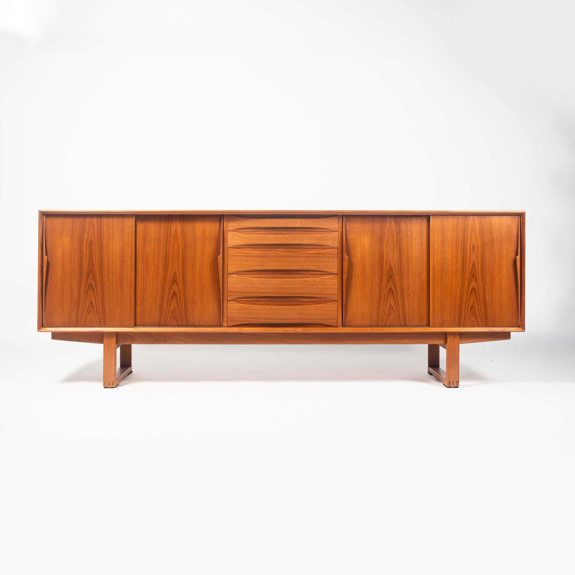 Dyrlund Danish teak credenza or sideboard with sled legs in the manner of Arne Vodder, circa 1960s. The credenza has five drawers and adjustable shelving for storage. Sculpted wood drawer pulls. with veneered back. Excellent condition.
 
